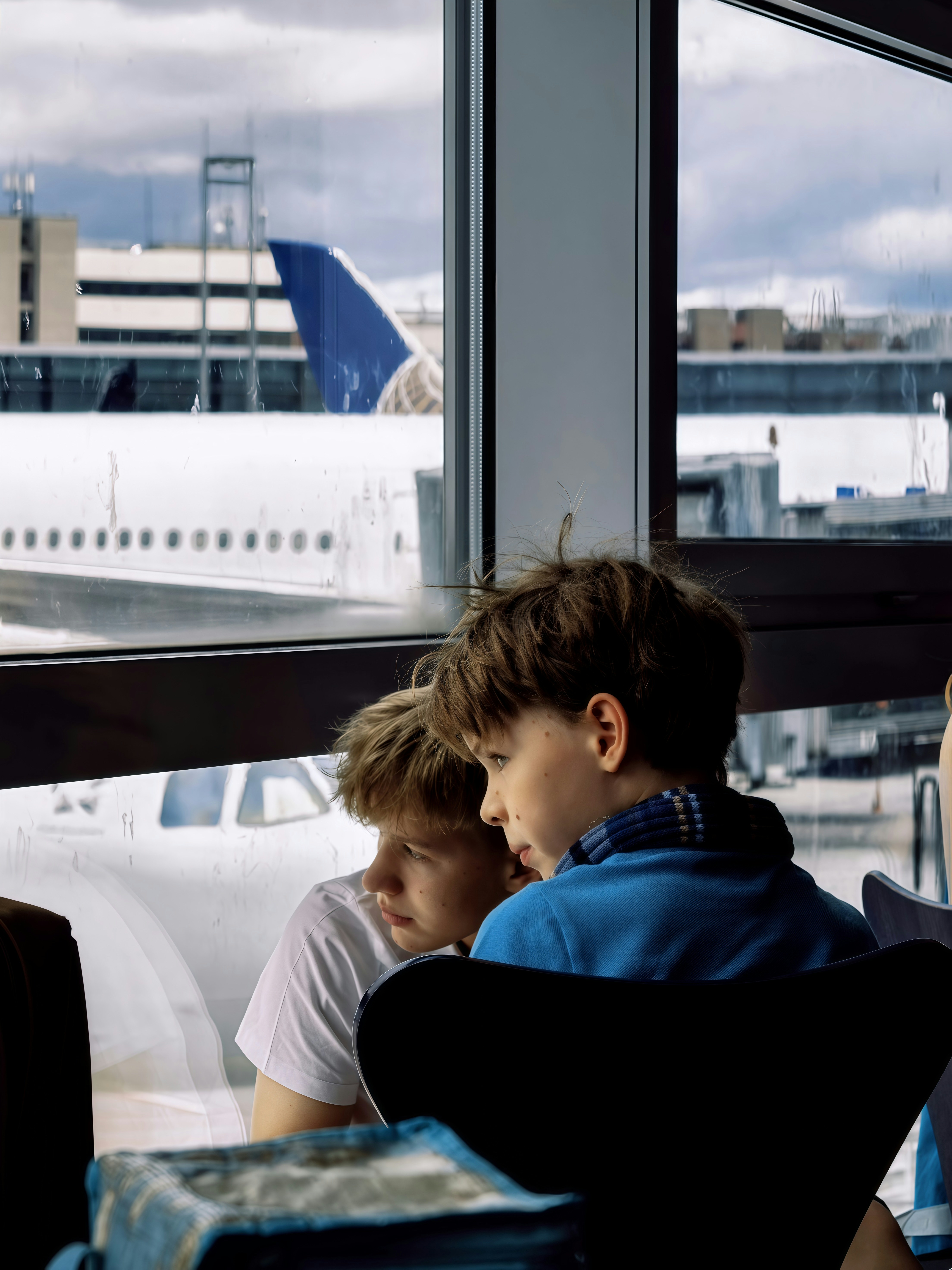 Two boys look out airport window at airplane.
