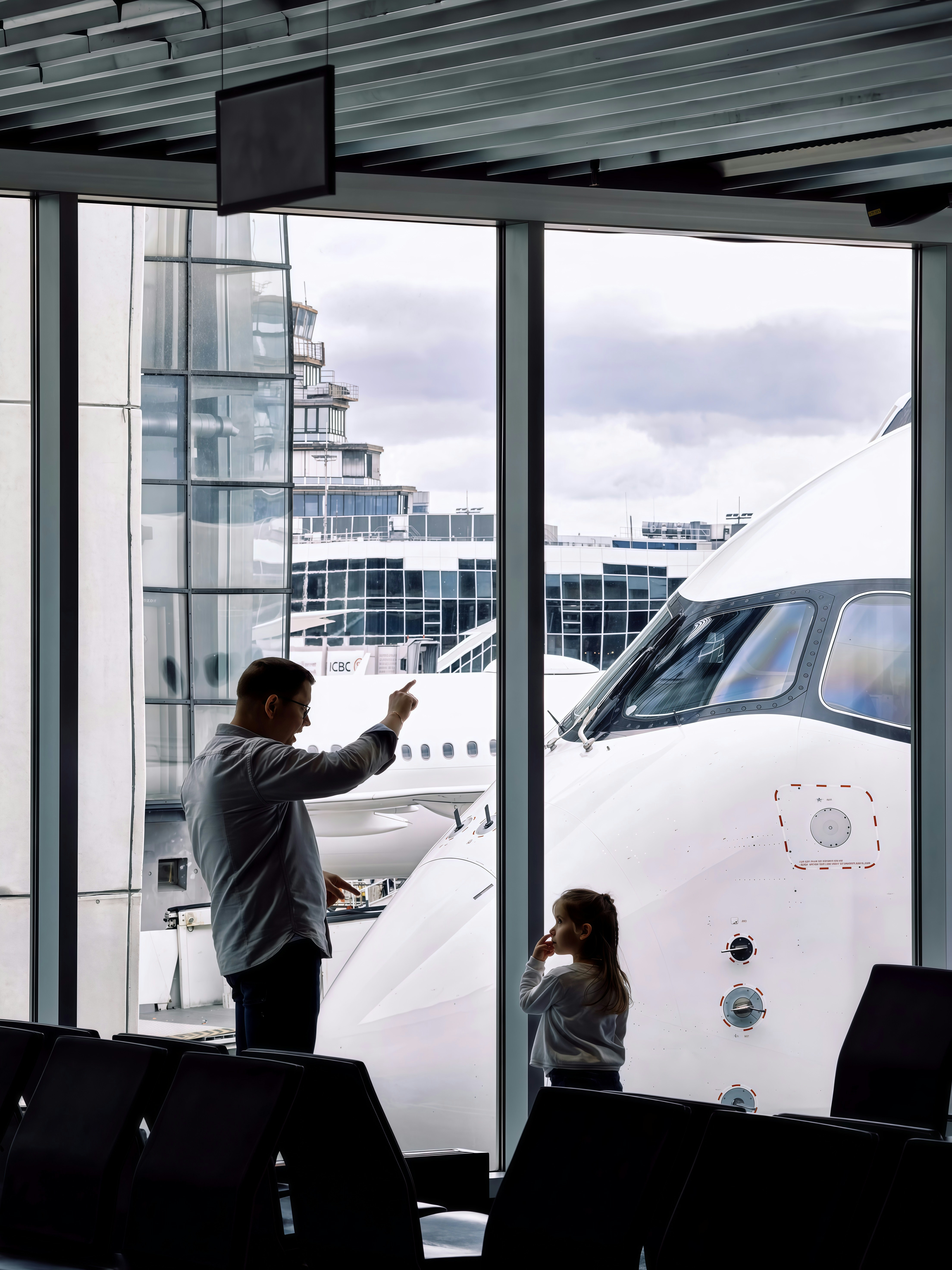 Father and daughter look at airplane at airport gate.