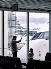 Father and daughter look at airplane at airport gate.