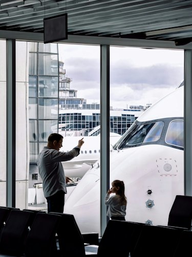 Family with young kids and rolling suitcases walking together through an airport terminal