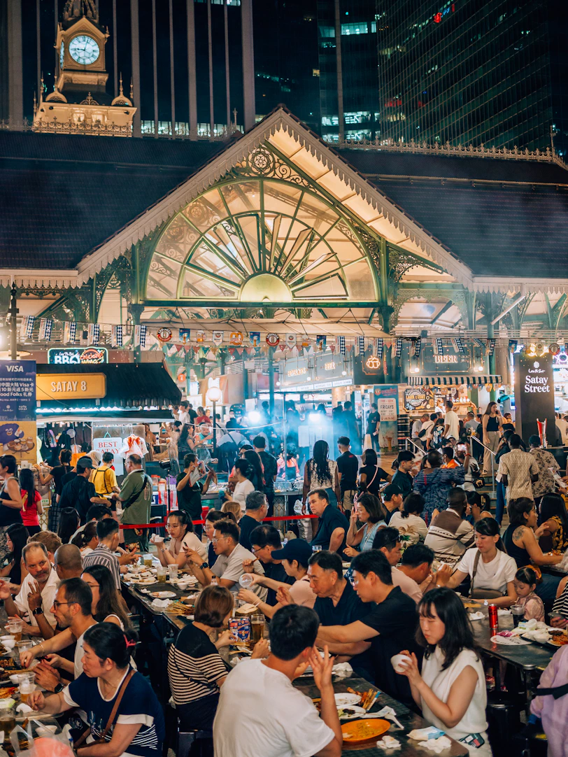 Crowded outdoor market with people eating at tables.