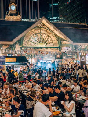 Crowded outdoor market with people eating at tables.