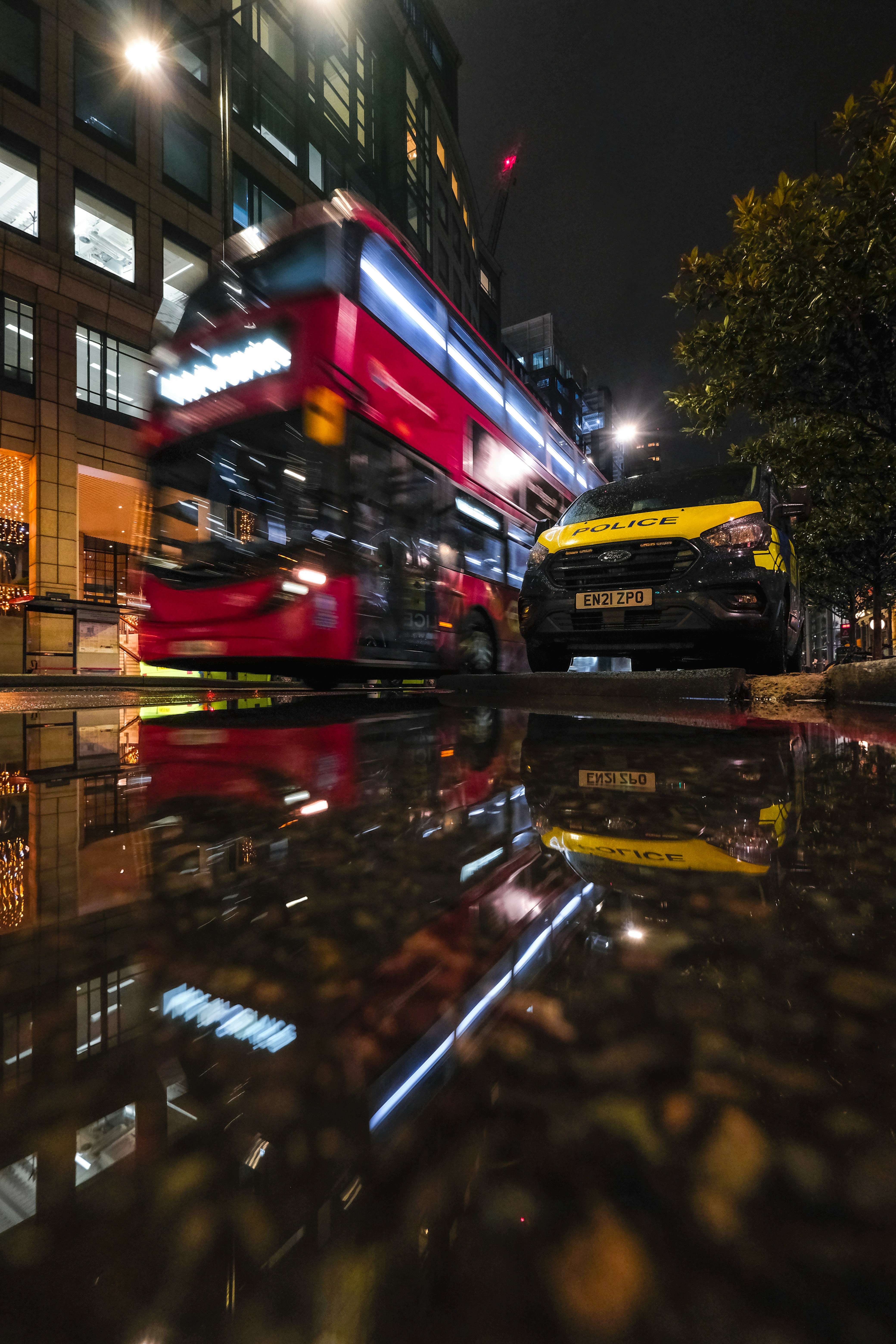 Red double-decker bus and police van at night