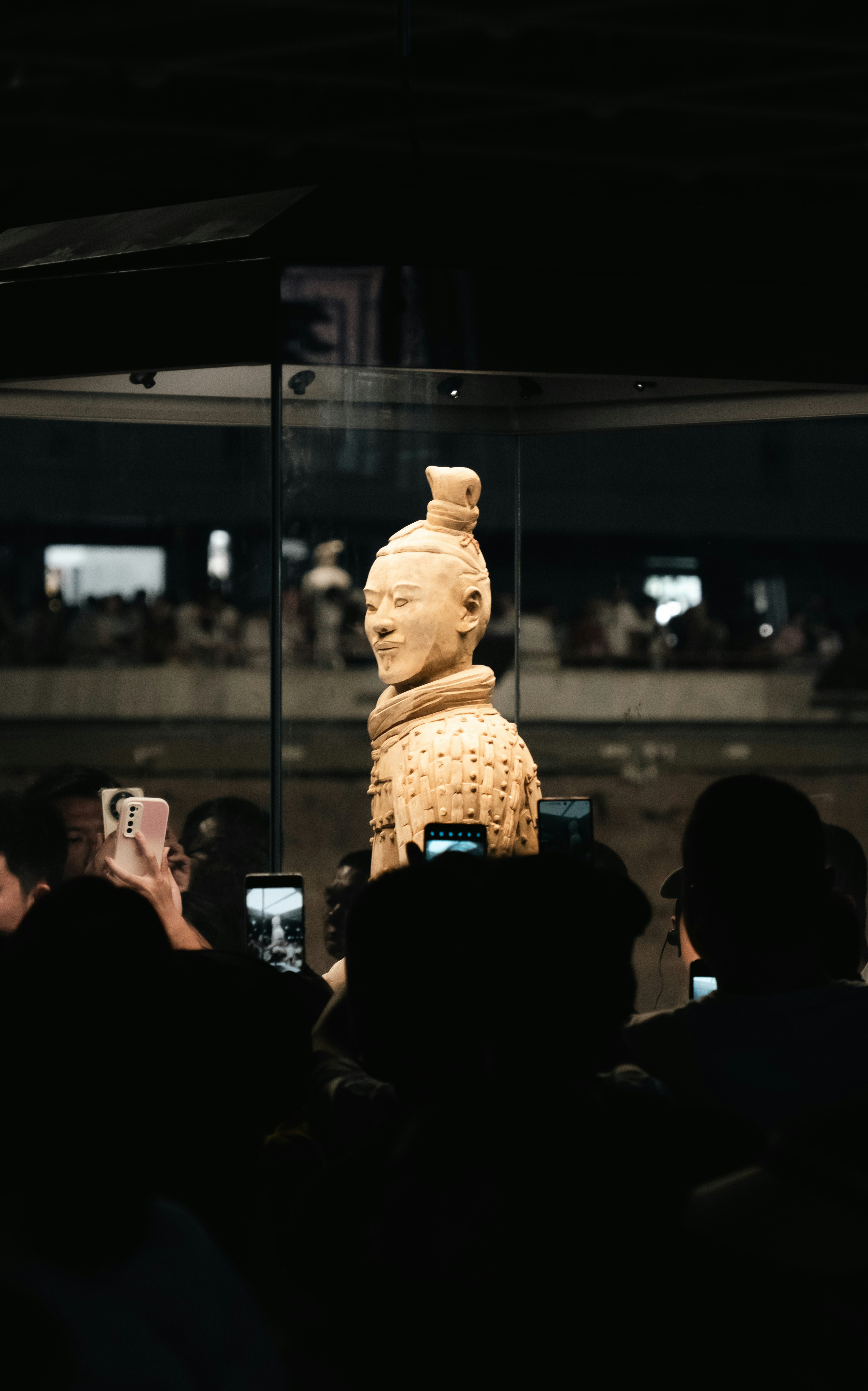 Terracotta warrior statue displayed behind glass with onlookers