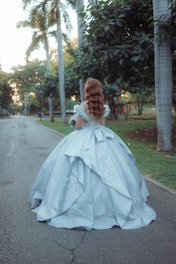 Woman in a light blue ballgown walking in a park.