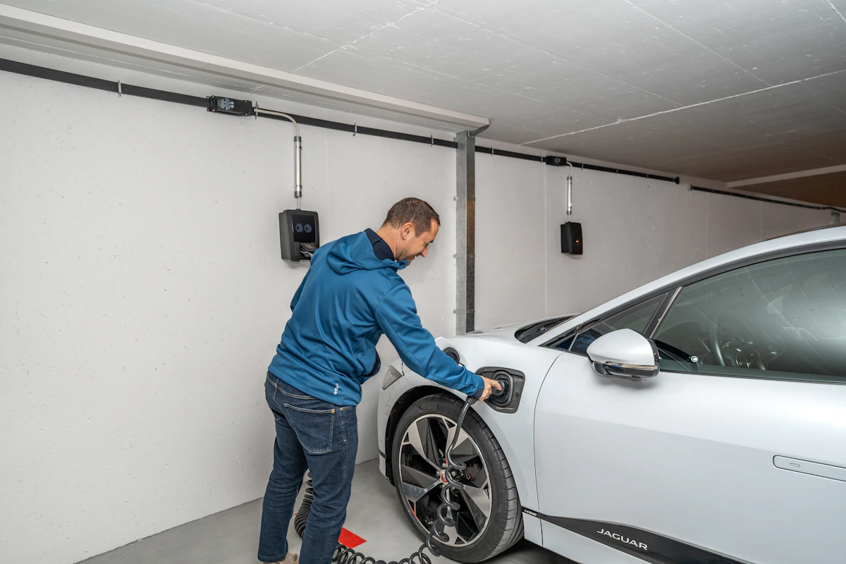 Ampersand Electric: A man plugging an EV charger into a white car in a bright garage