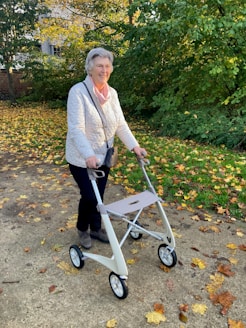 Elderly woman walking with a walker in autumn park.