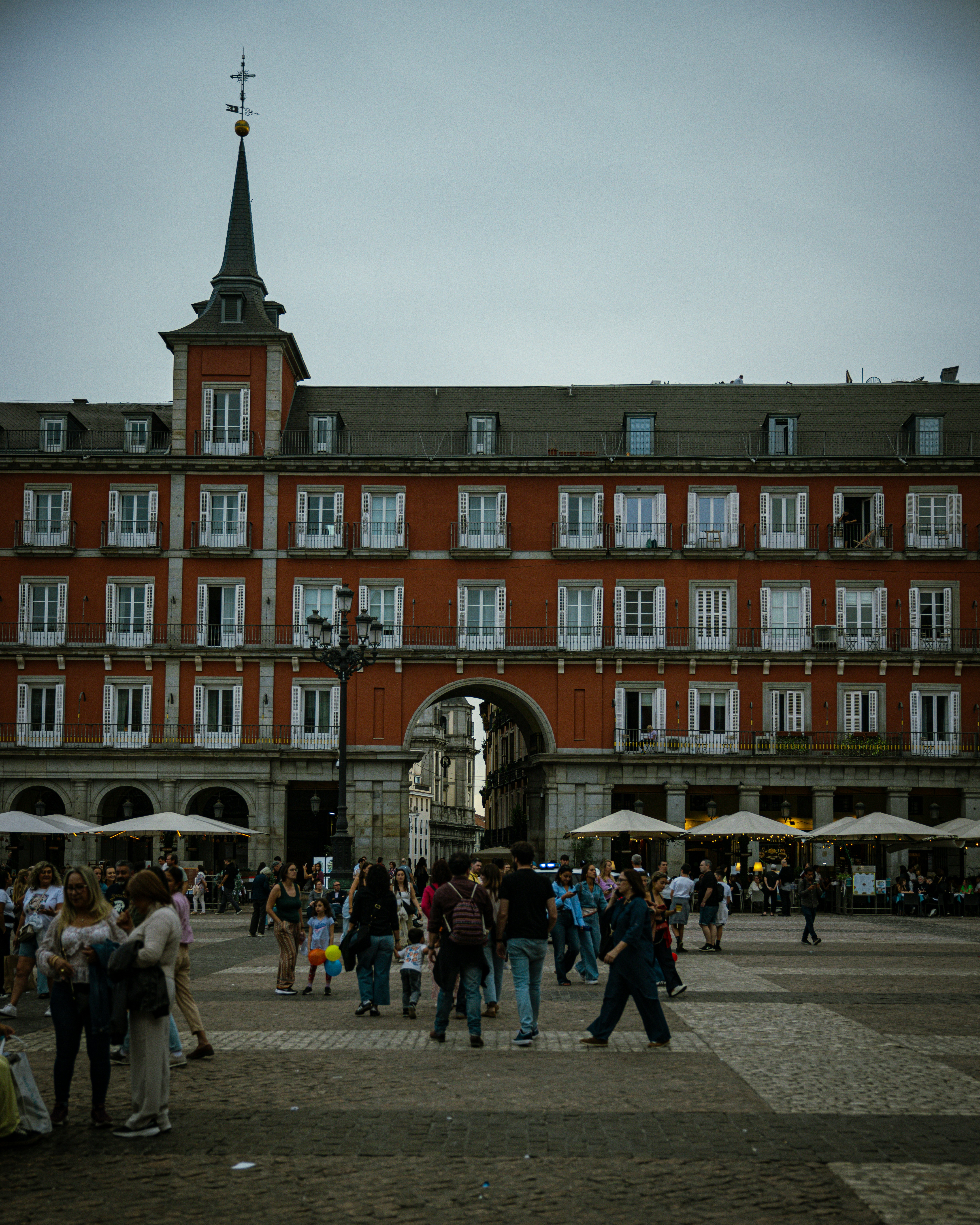 People gather in a plaza with a large red building.