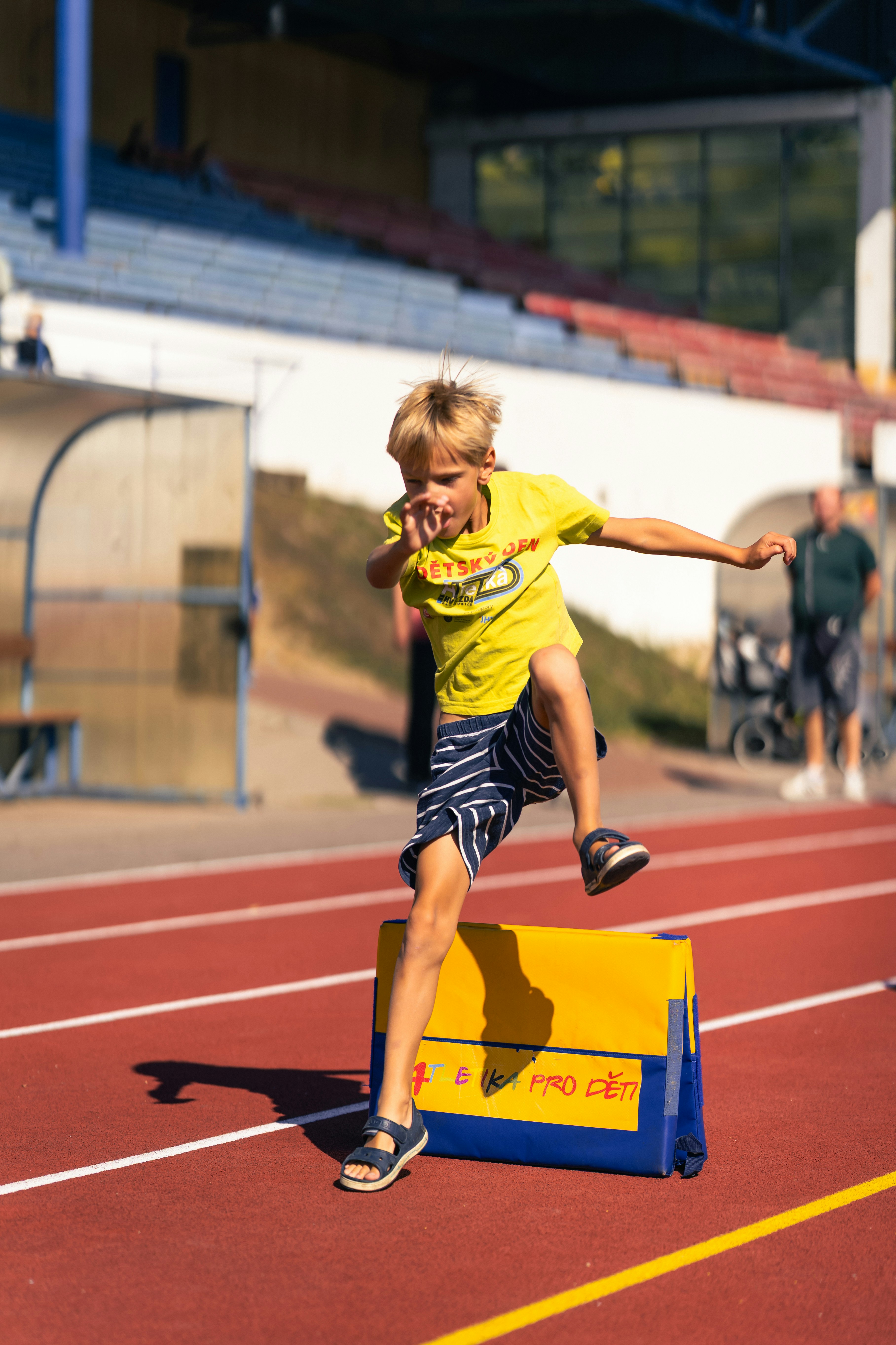 A young boy jumps over a hurdle on a track.