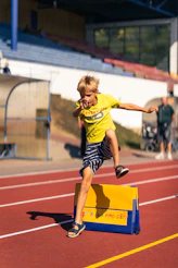 A young boy jumps over a hurdle on a track