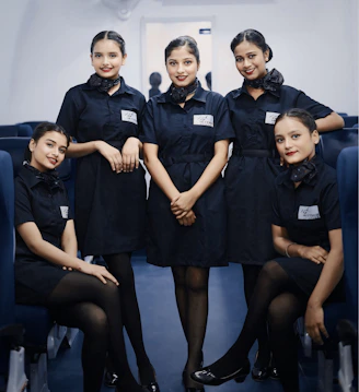 Five women in dark blue uniforms inside airplane
