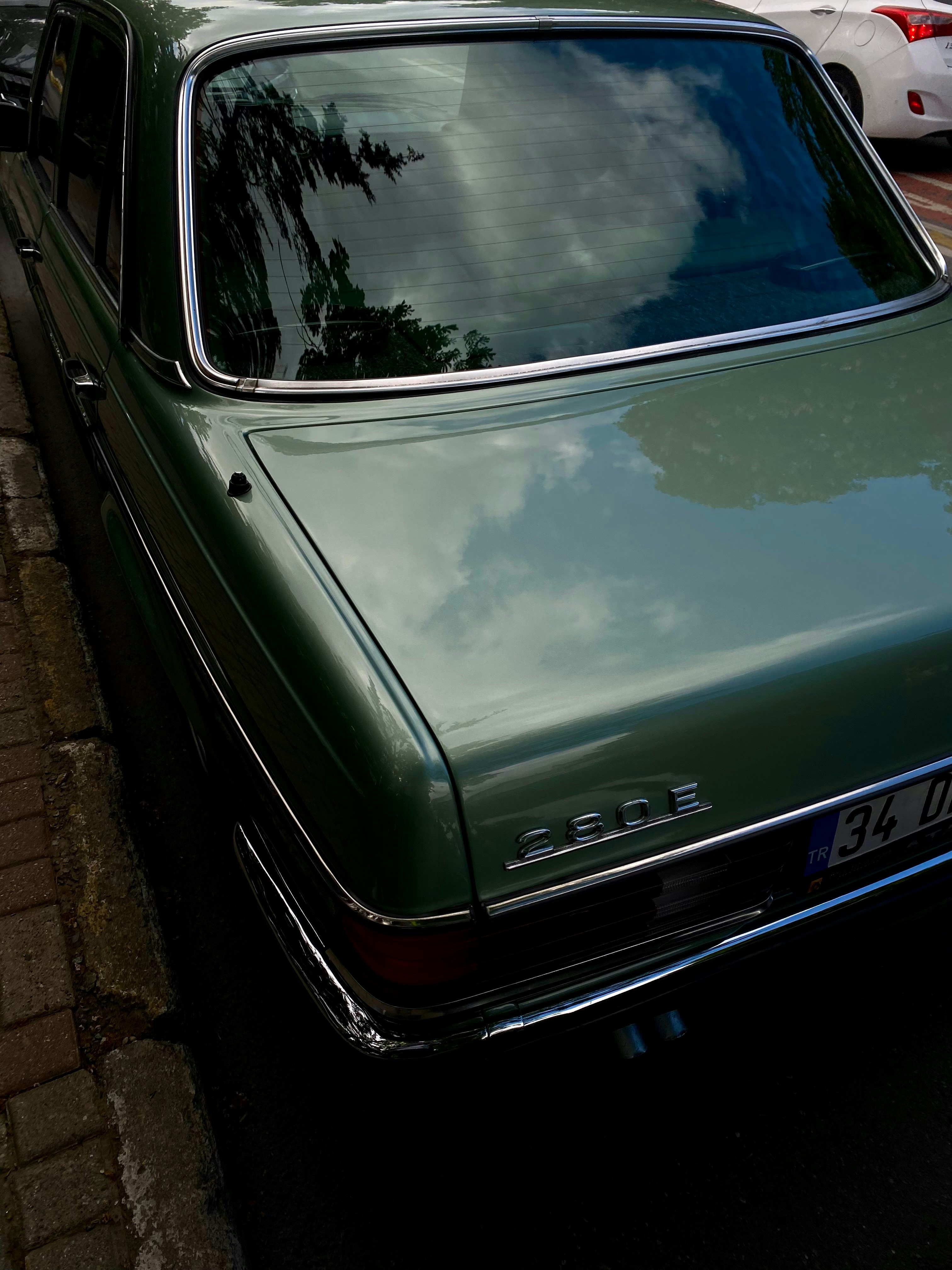 Green vintage car parked on a brick sidewalk.