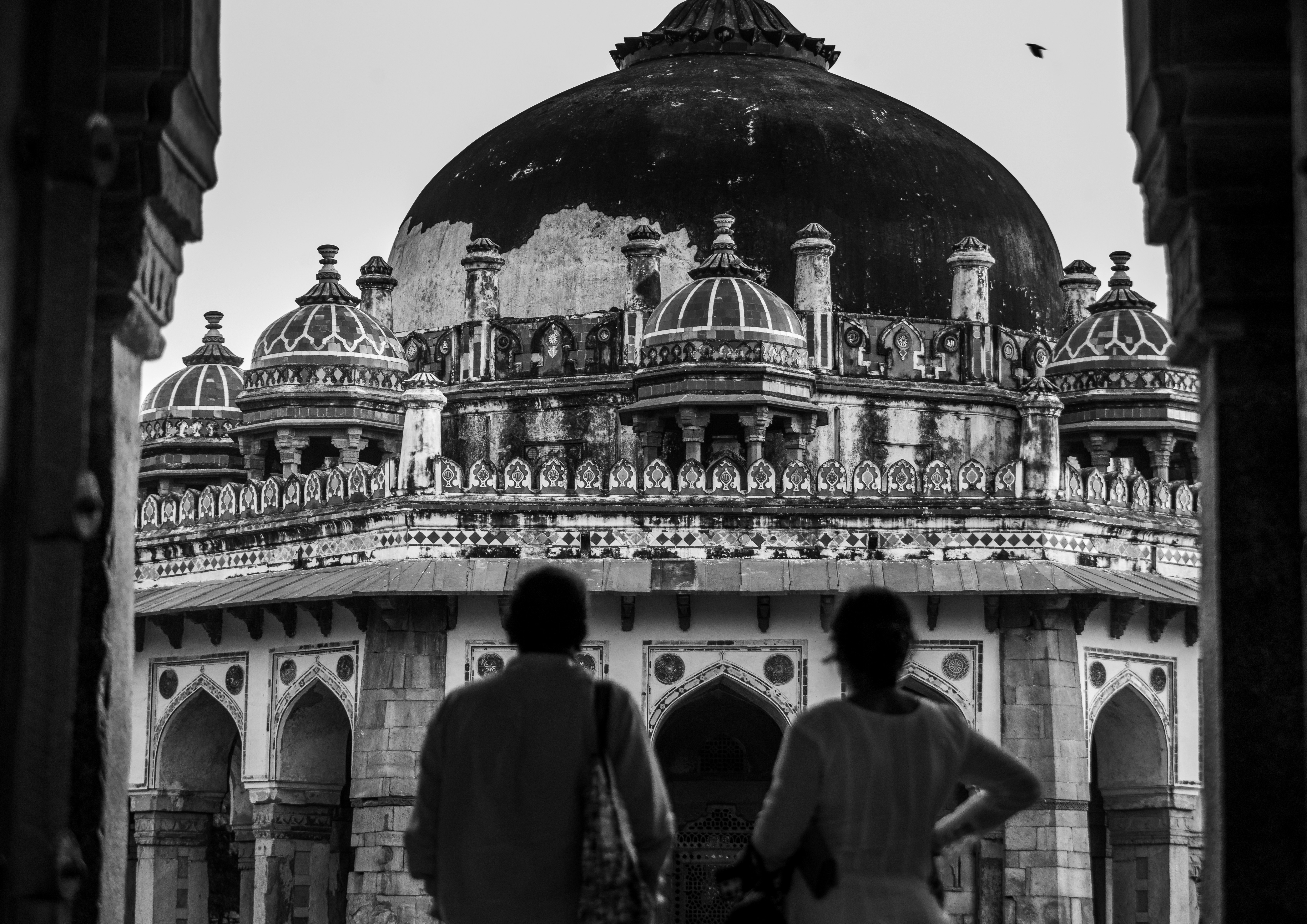 A man and woman stand in an arched doorway admiring the beauty of Isa Khan's Tomb