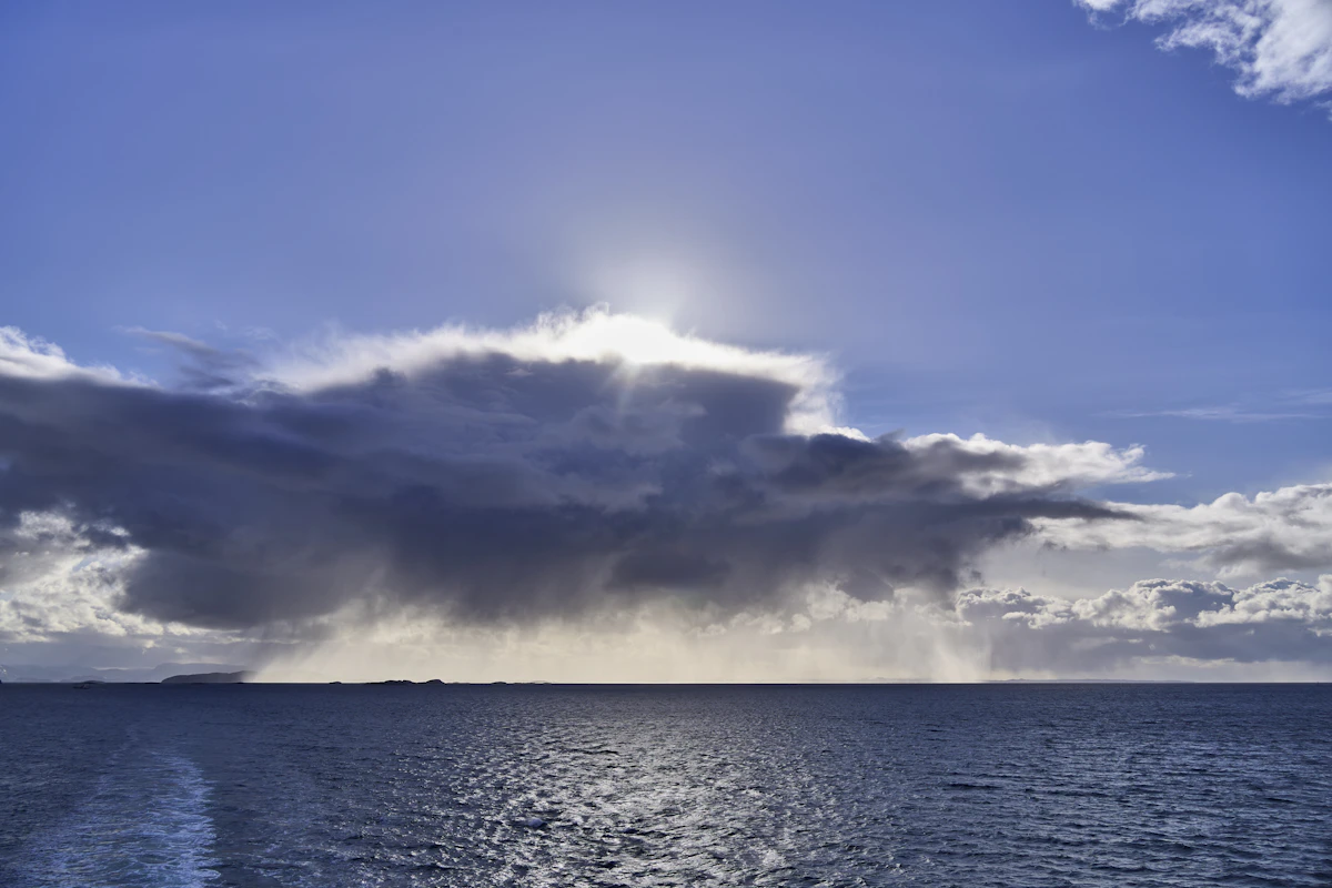 Sunlight breaking through storm clouds over calm ocean water, representing the period after a storm system passes without making landfall