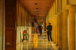 People walking down a long, sunlit hallway with columns.