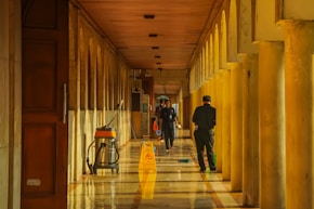 People walking down a long, sunlit hallway with columns.