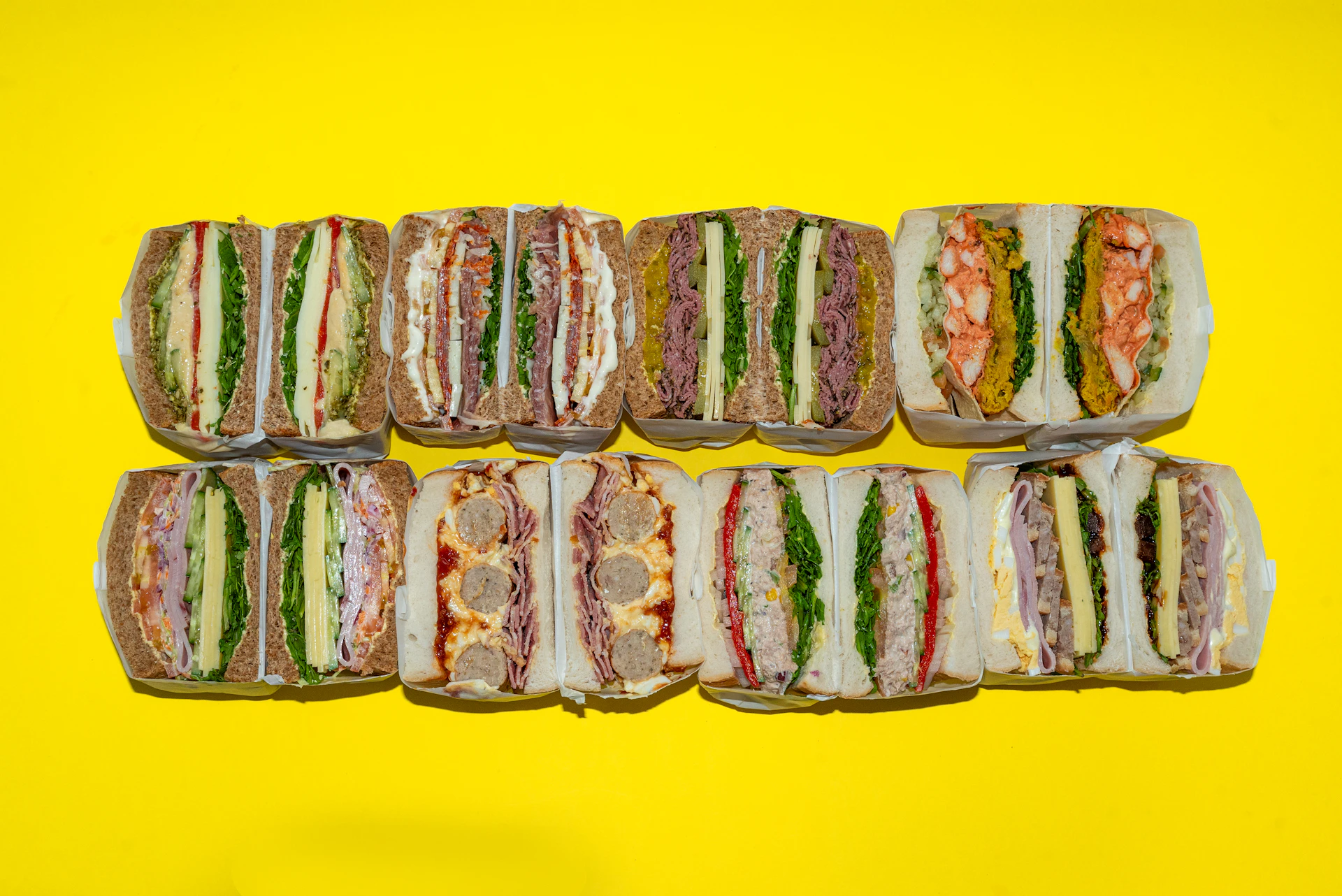 Assortment of eight layered sandwiches on yellow background