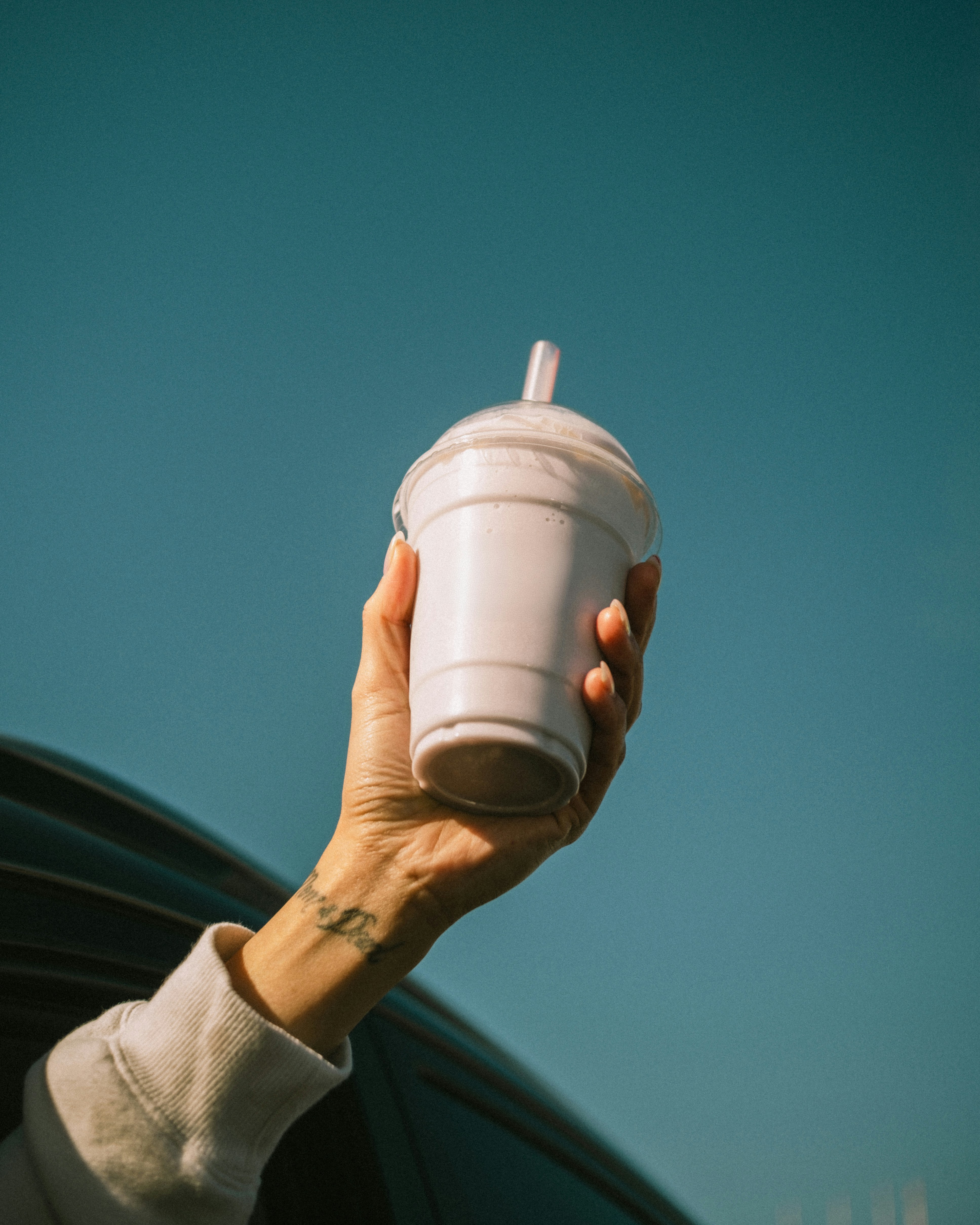 Hand holding a milkshake out of car window