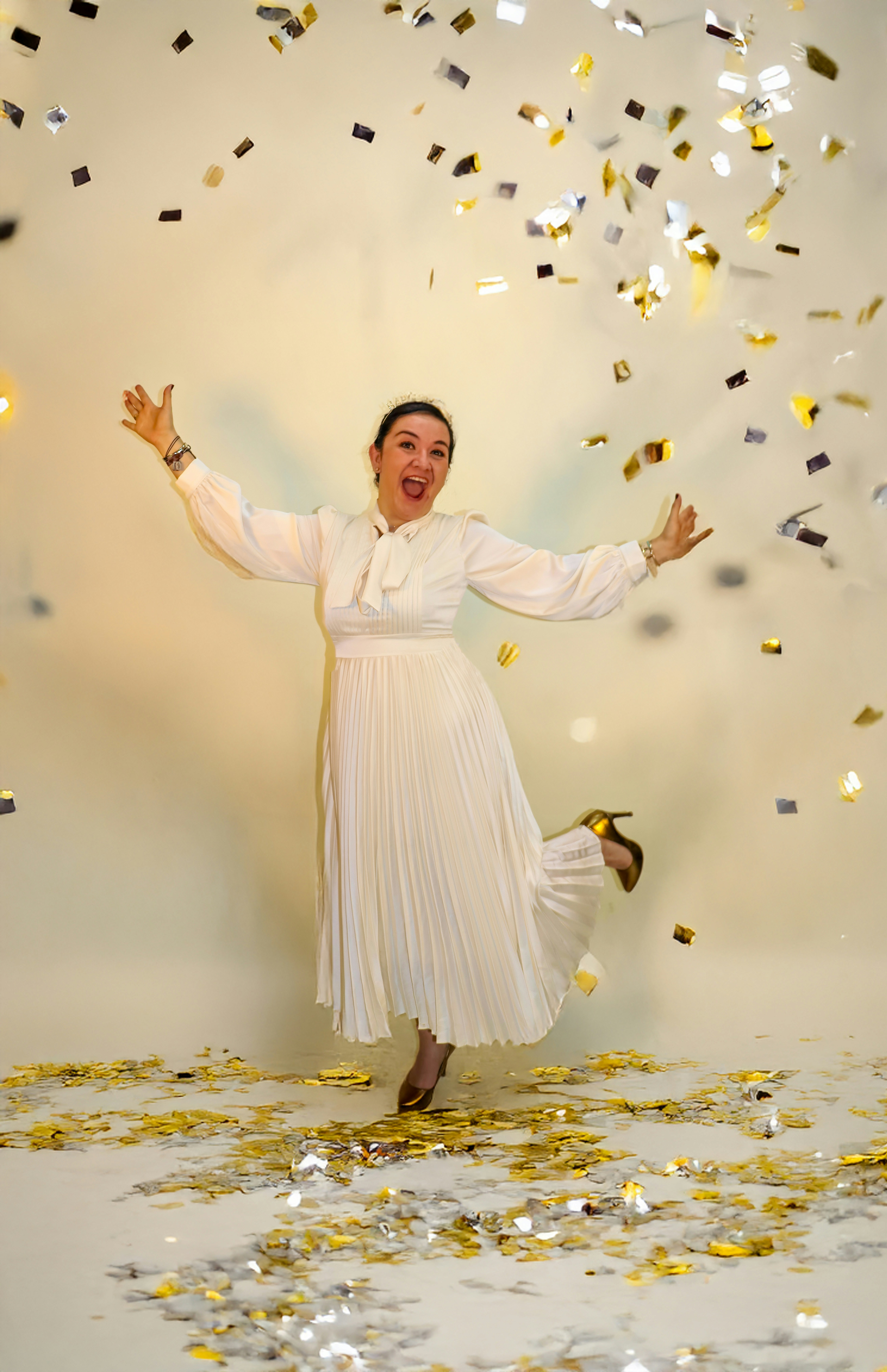 Frau im weißen Kleid feiert mit herabfallendem Konfetti.