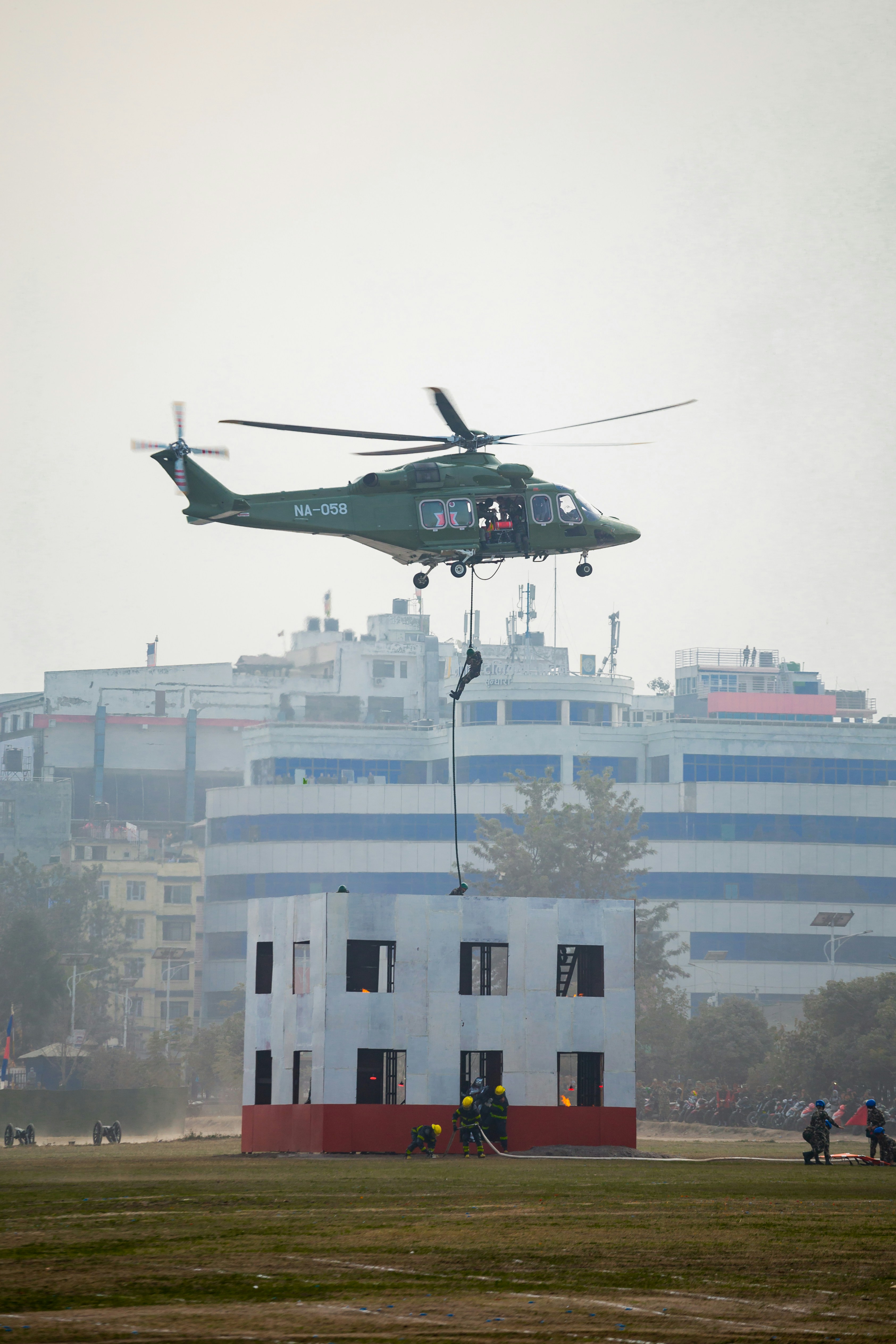 Helicopter rappels rescuer near simulated building.