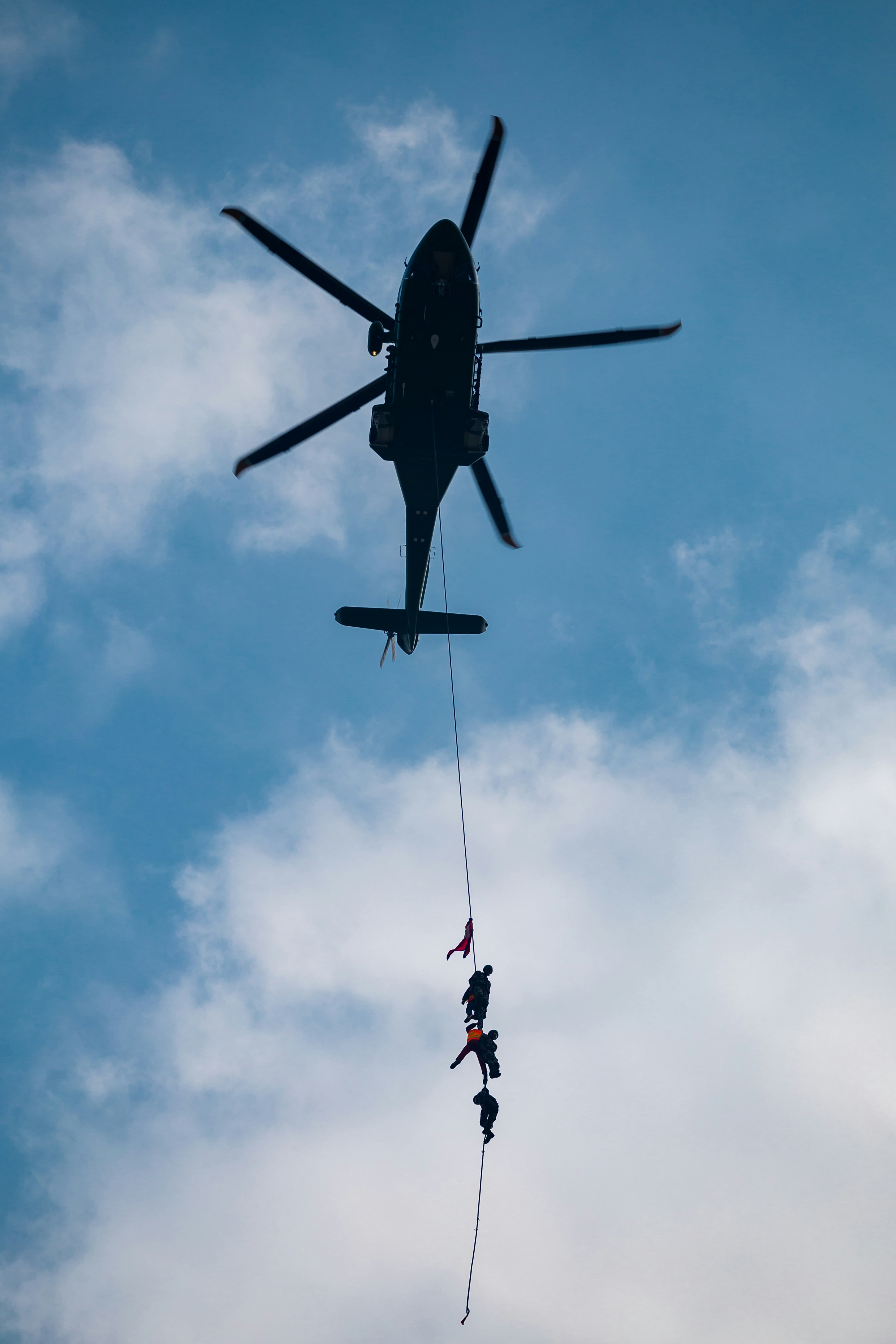 Helicopter carrying people suspended by rope.