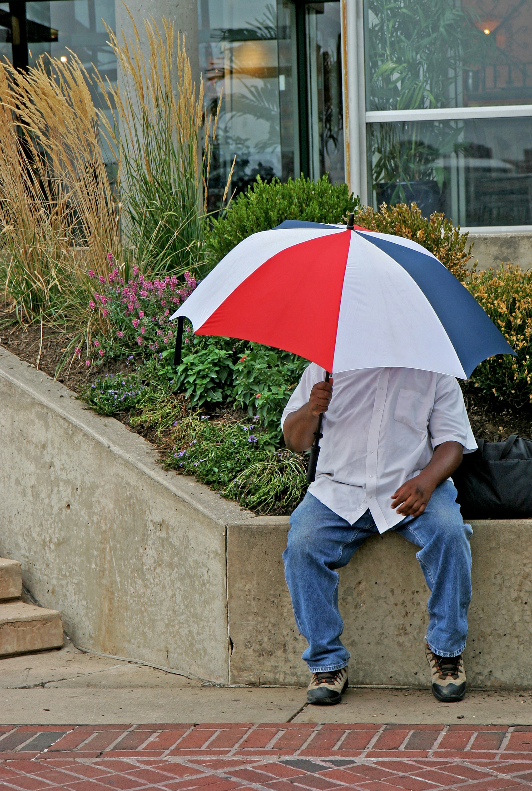 Hombre con paraguas sentado en el borde de hormigón