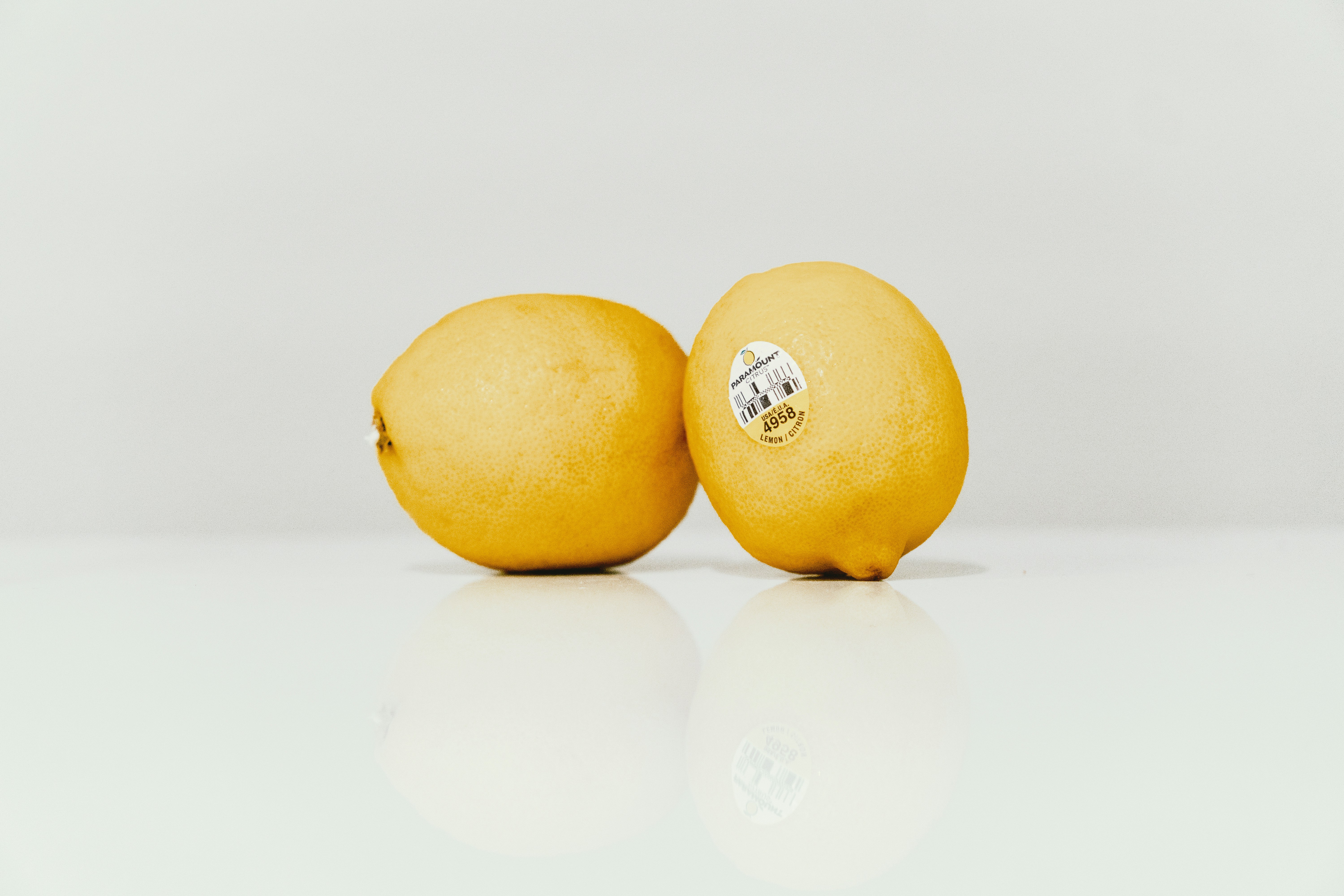 Two yellow lemons on a white surface