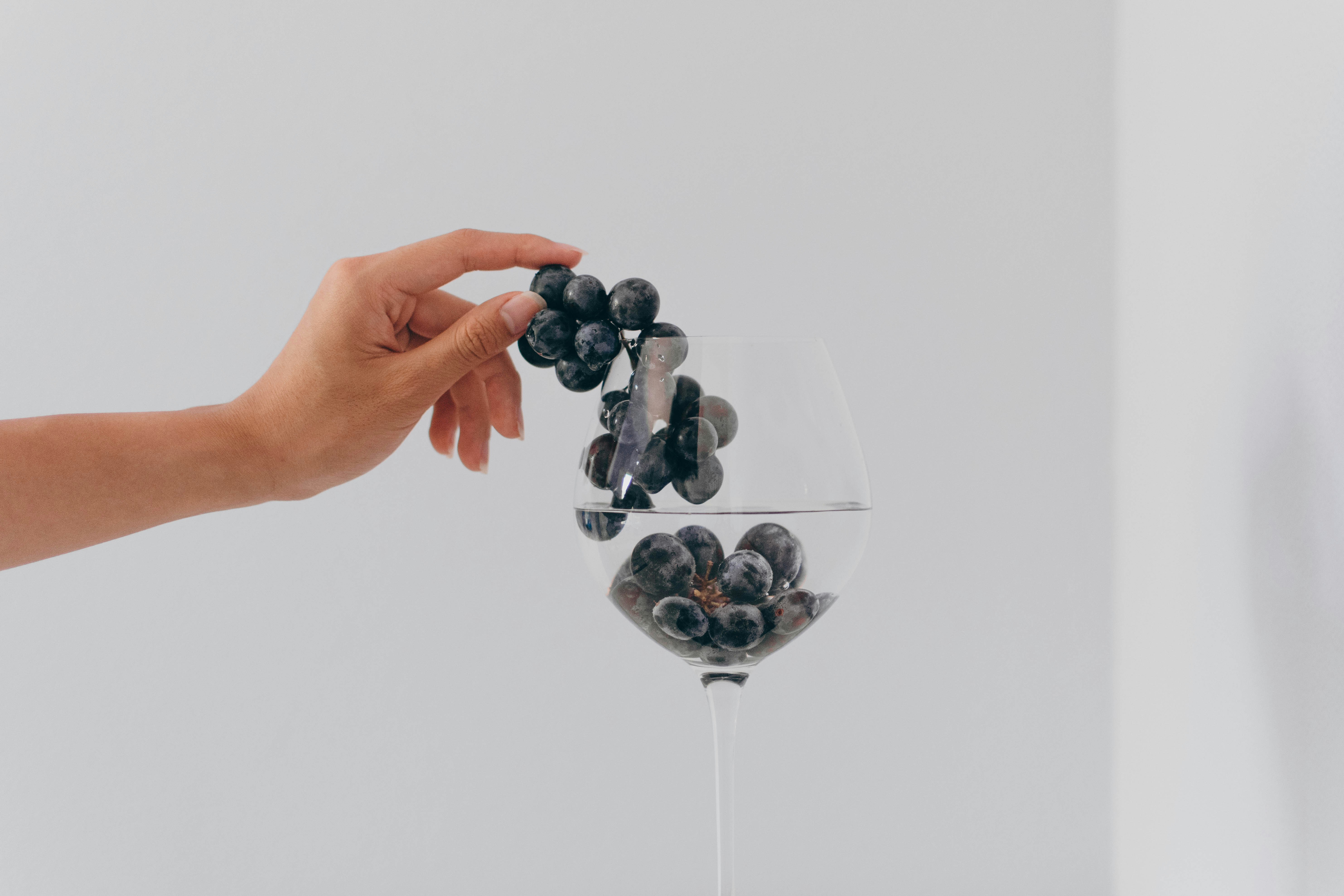 Hand placing grapes into a wine glass