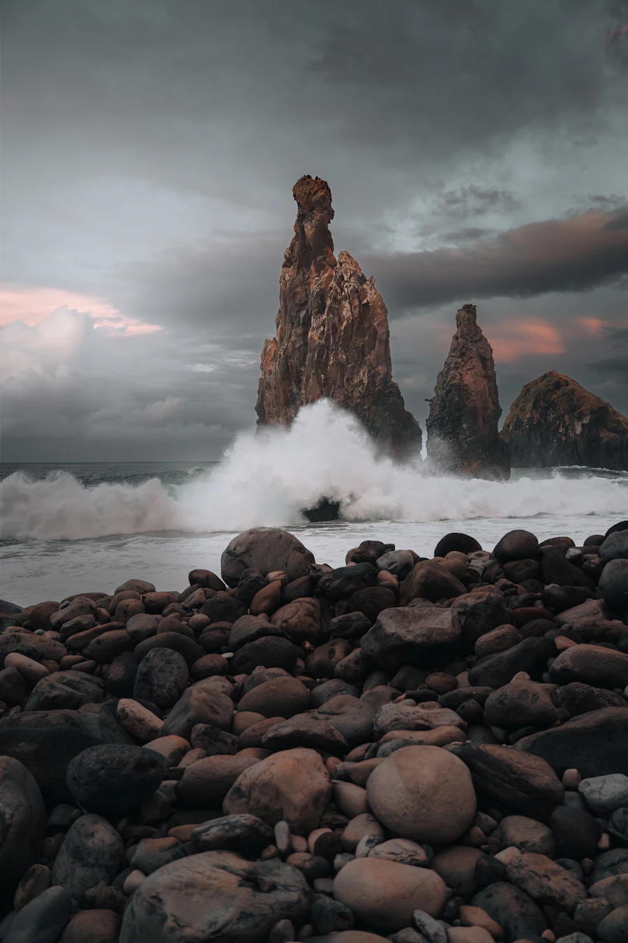 Dramatic Pacific waves crashing against rocky coastal sea stacks under a dark cloudy sky