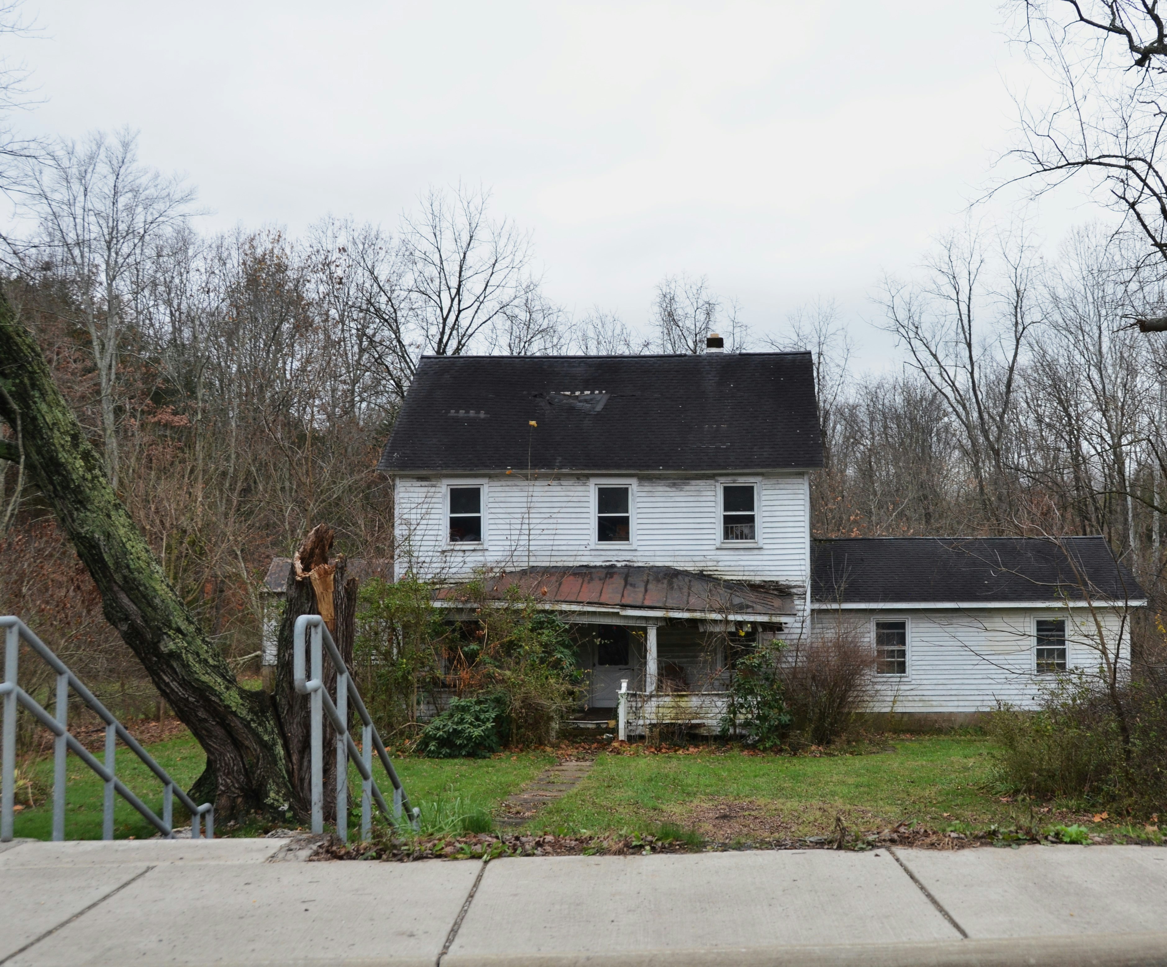 An abandoned white house surrounded by trees