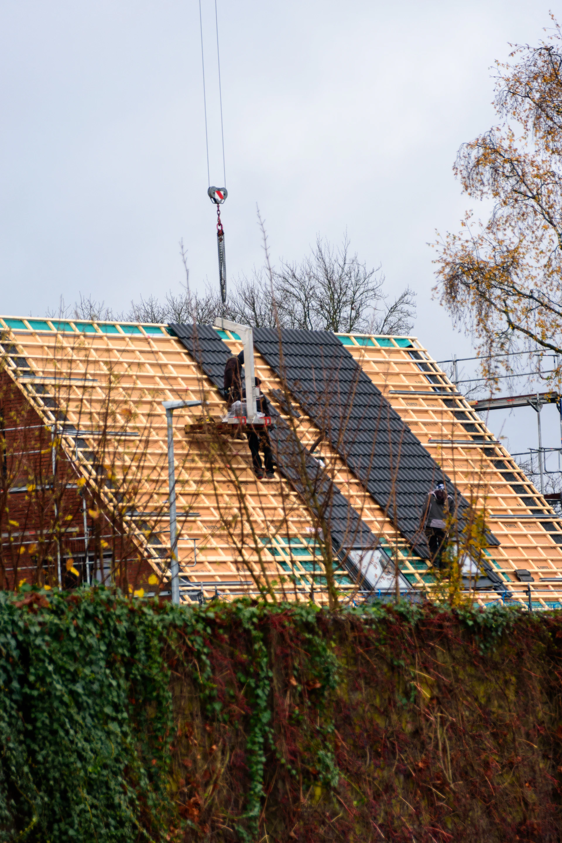 Workers installing roofing tiles on a house under-construction house.