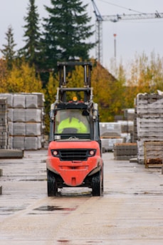 Red forklift driving on a wet construction site.