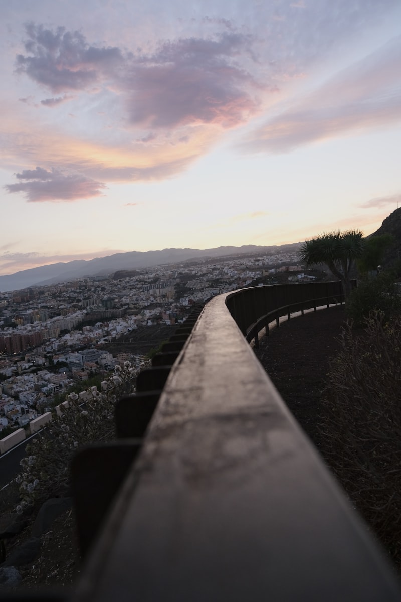 Paisaje urbano al atardecer con una barandilla en primer plano.