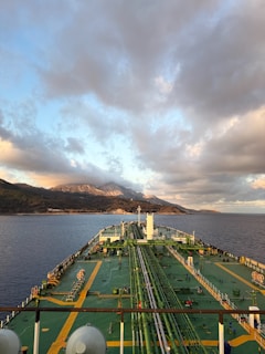 Tanker ship sailing towards mountains under cloudy sky
