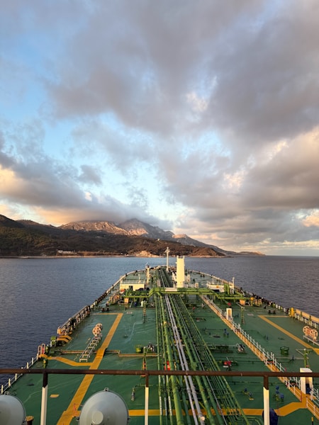 Tanker ship sailing towards mountains under cloudy sky