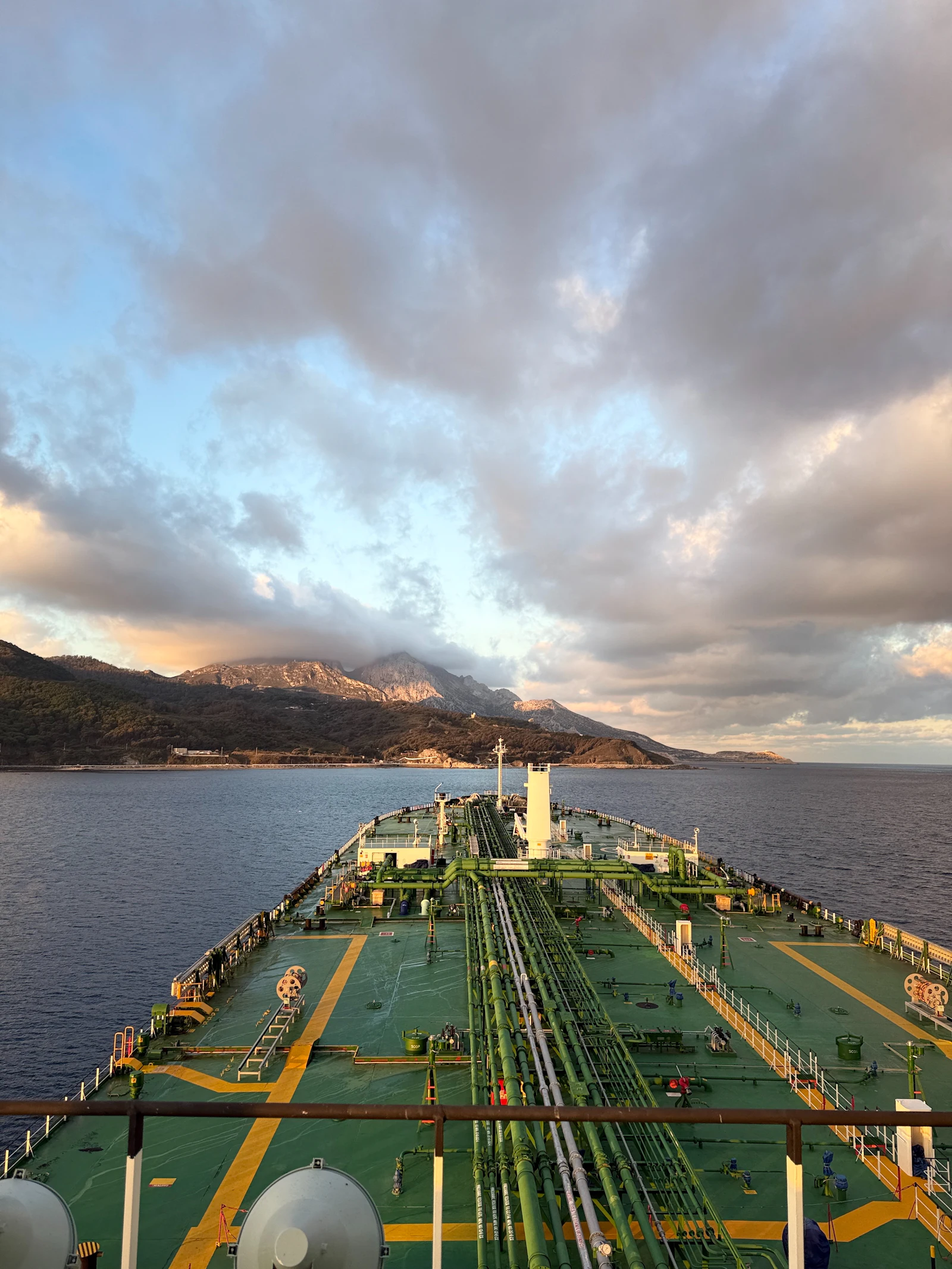A crude oil tanker sailing toward mountains under a cloudy sky