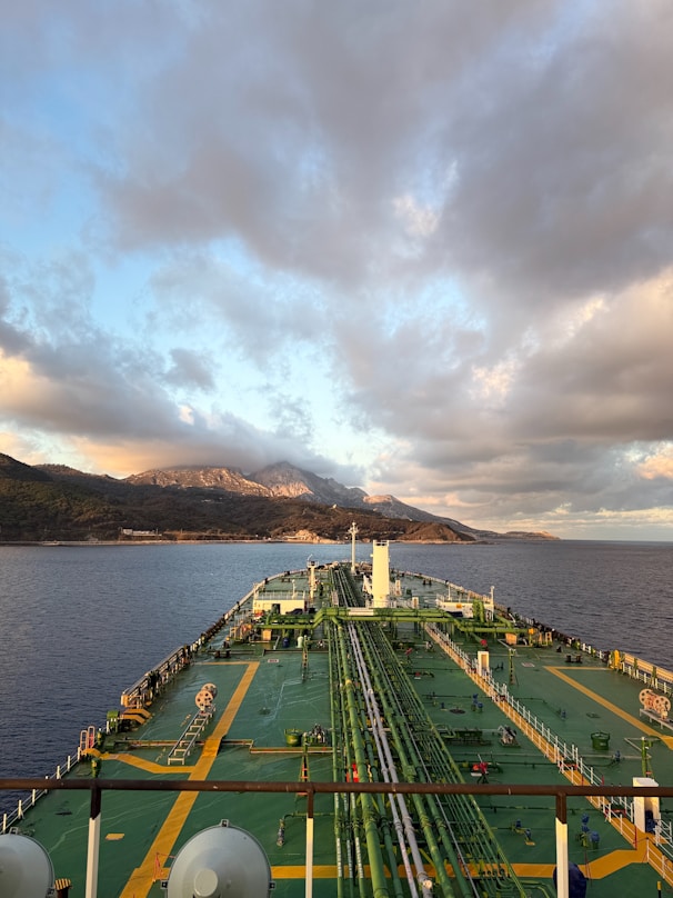 Tanker ship sailing towards mountains under cloudy sky