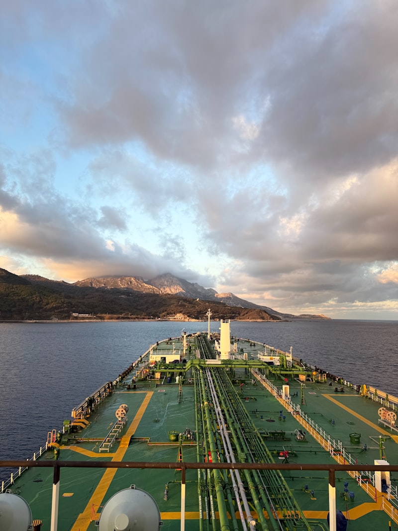 Tanker ship sailing toward mountains under a cloudy sky