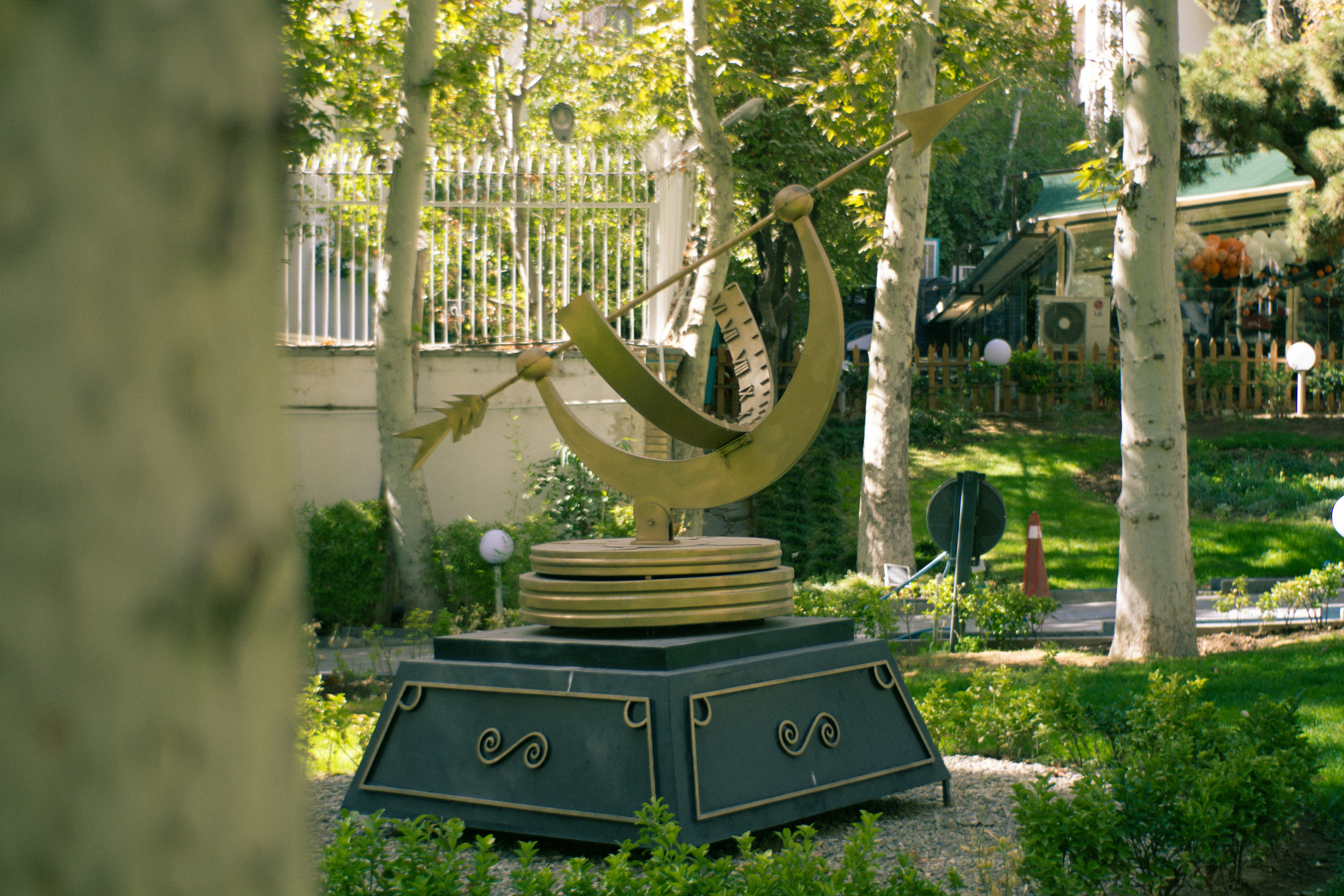 A golden sundial sculpture in a garden setting of park.
