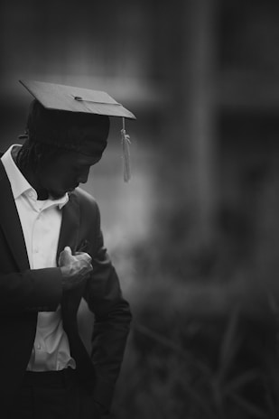A graduate in cap and gown looking down thoughtfully