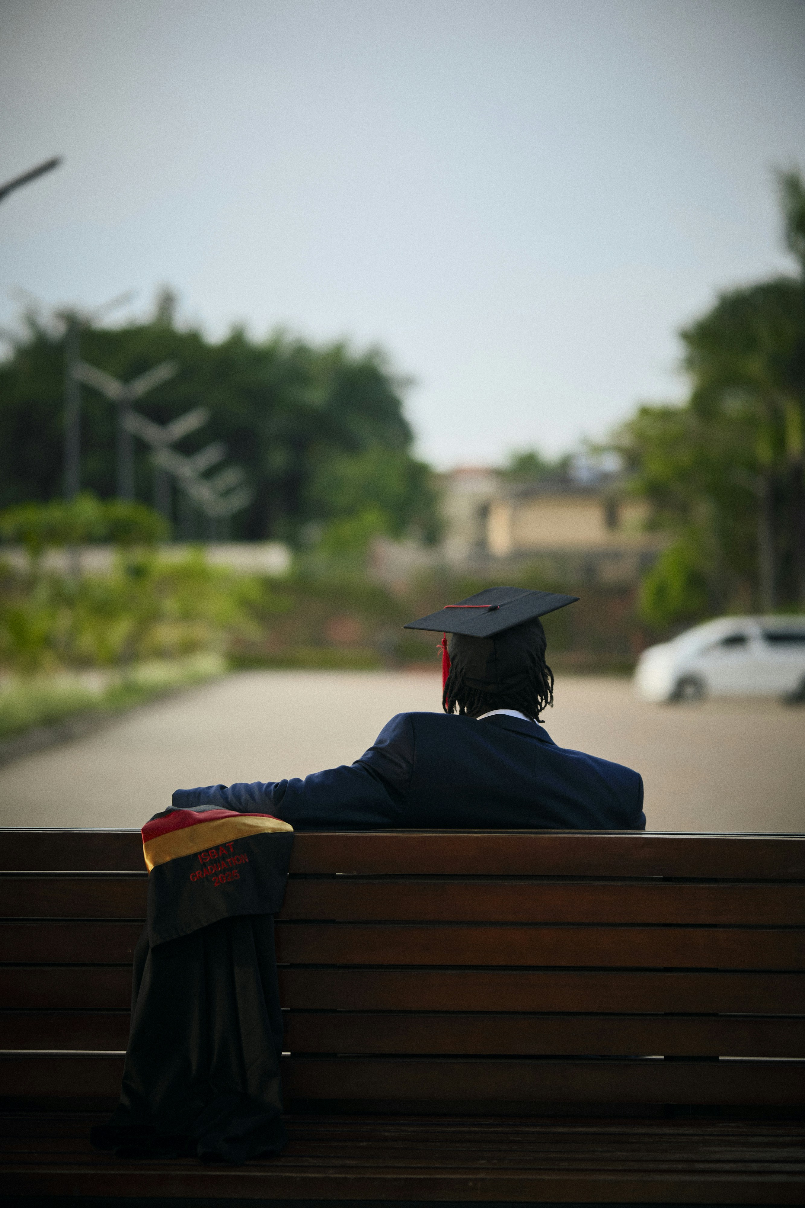 Graduate in cap and gown sits on a bench