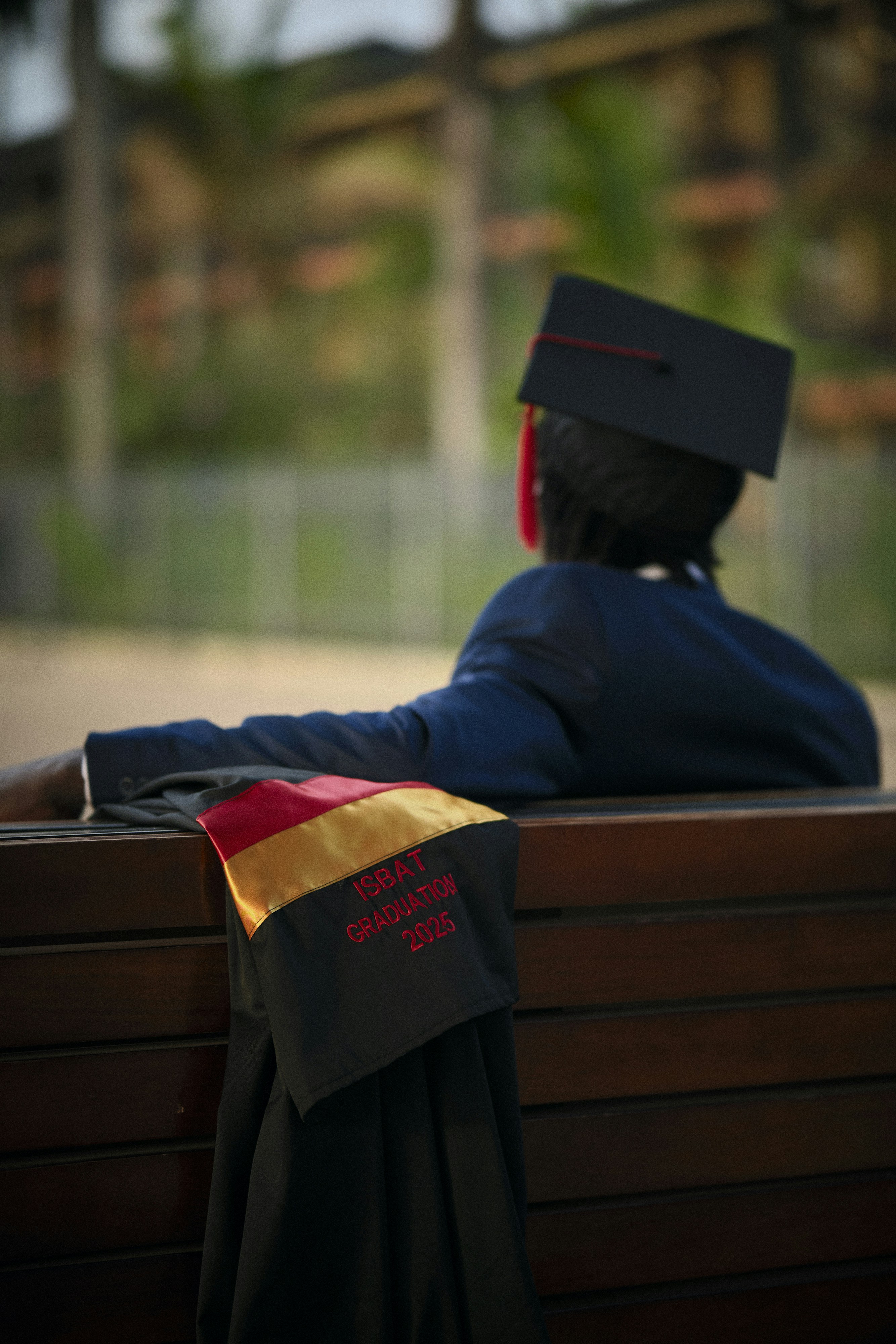 Person in graduation cap and gown on bench.