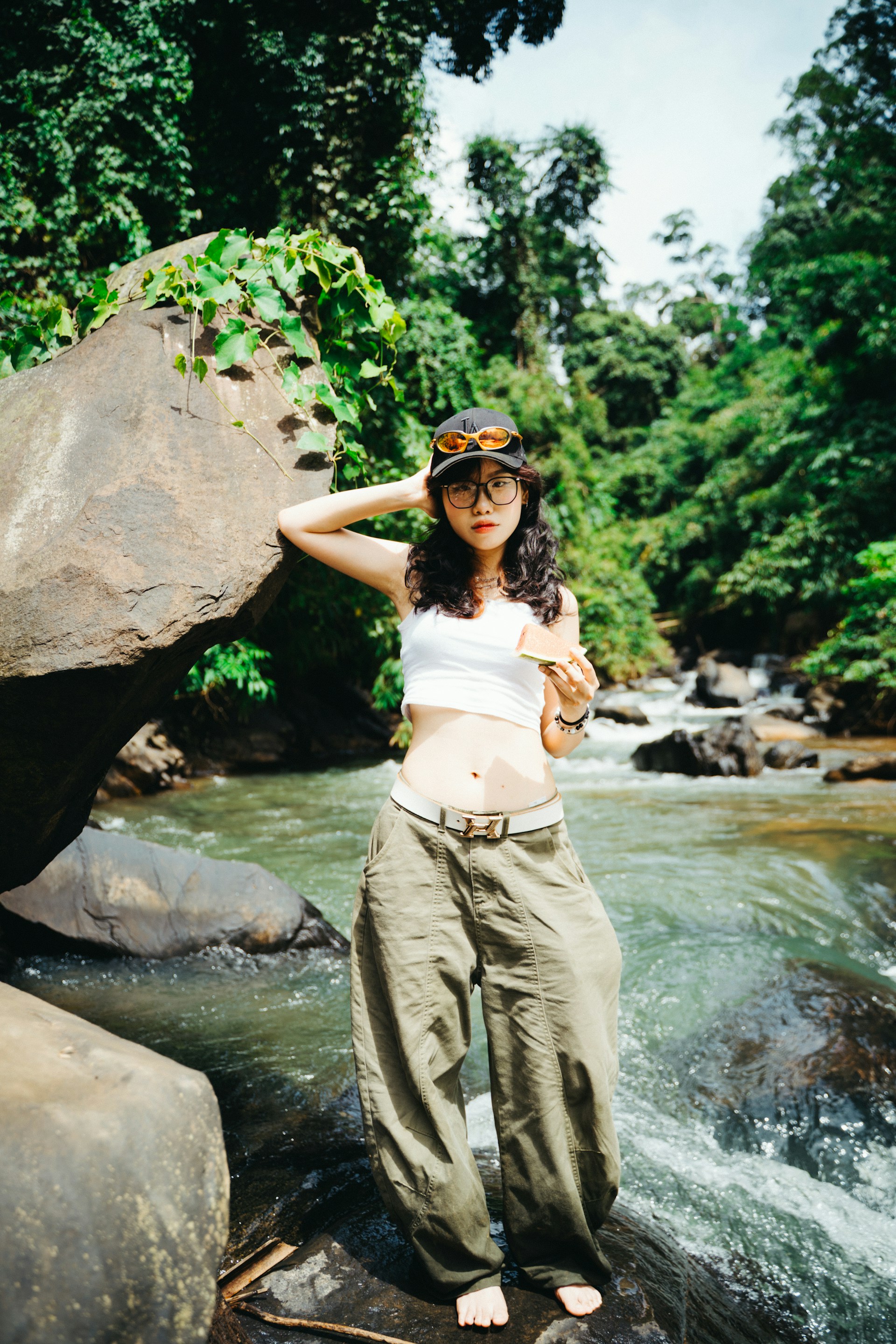 Woman posing by a rocky river in a lush forest.