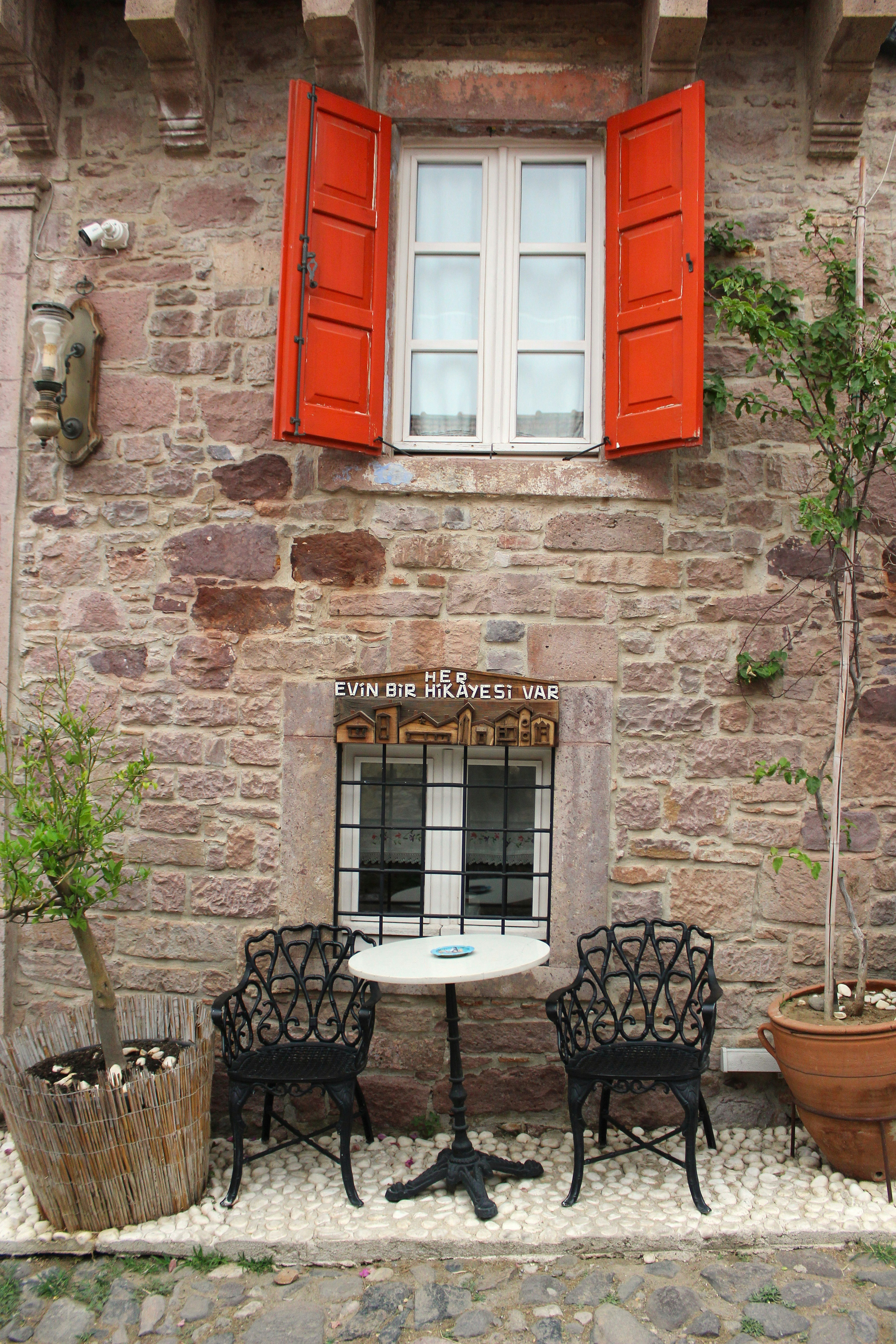 Stone building facade with open red shutters and seating area.