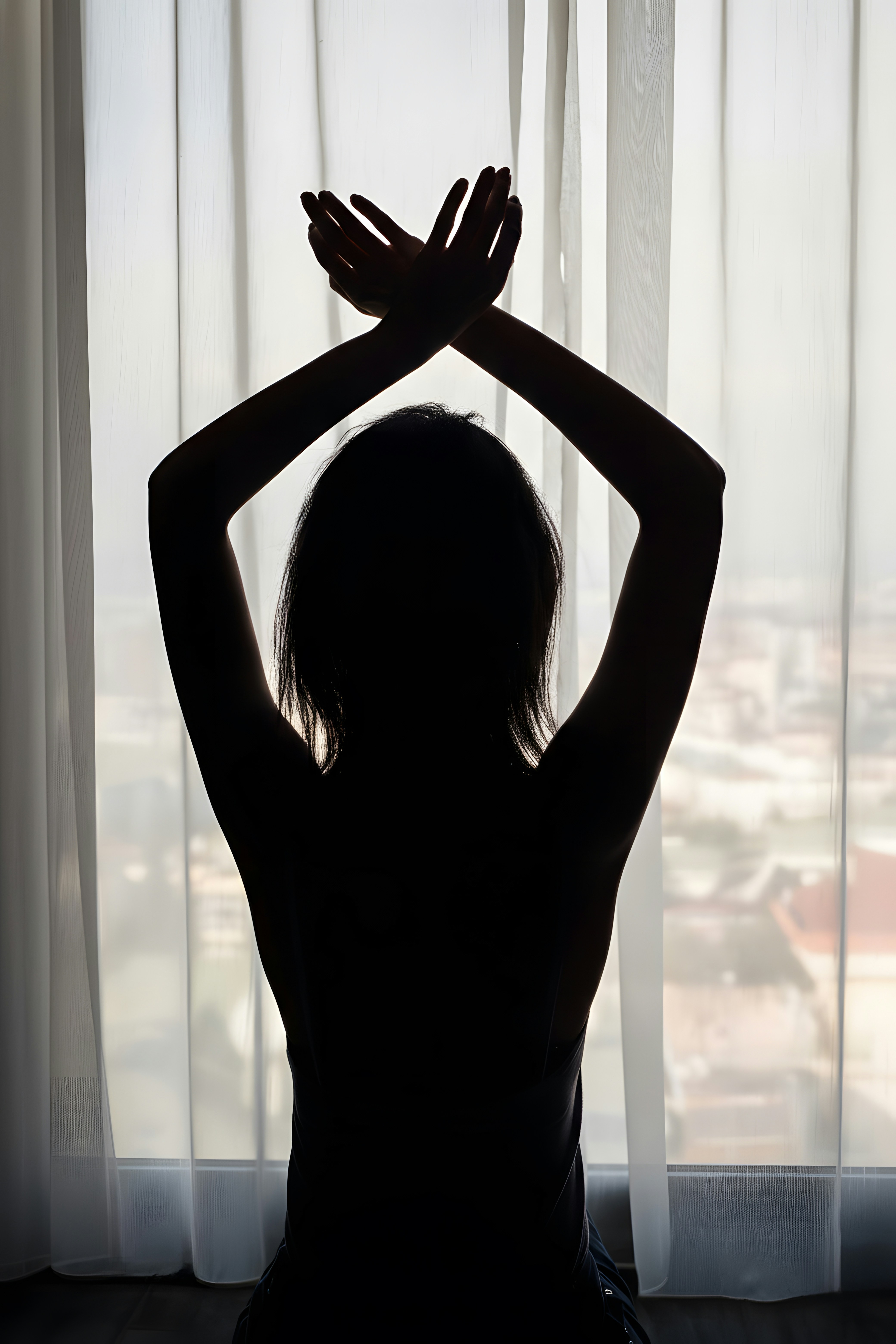 Silhouette of a woman with arms crossed overhead.
