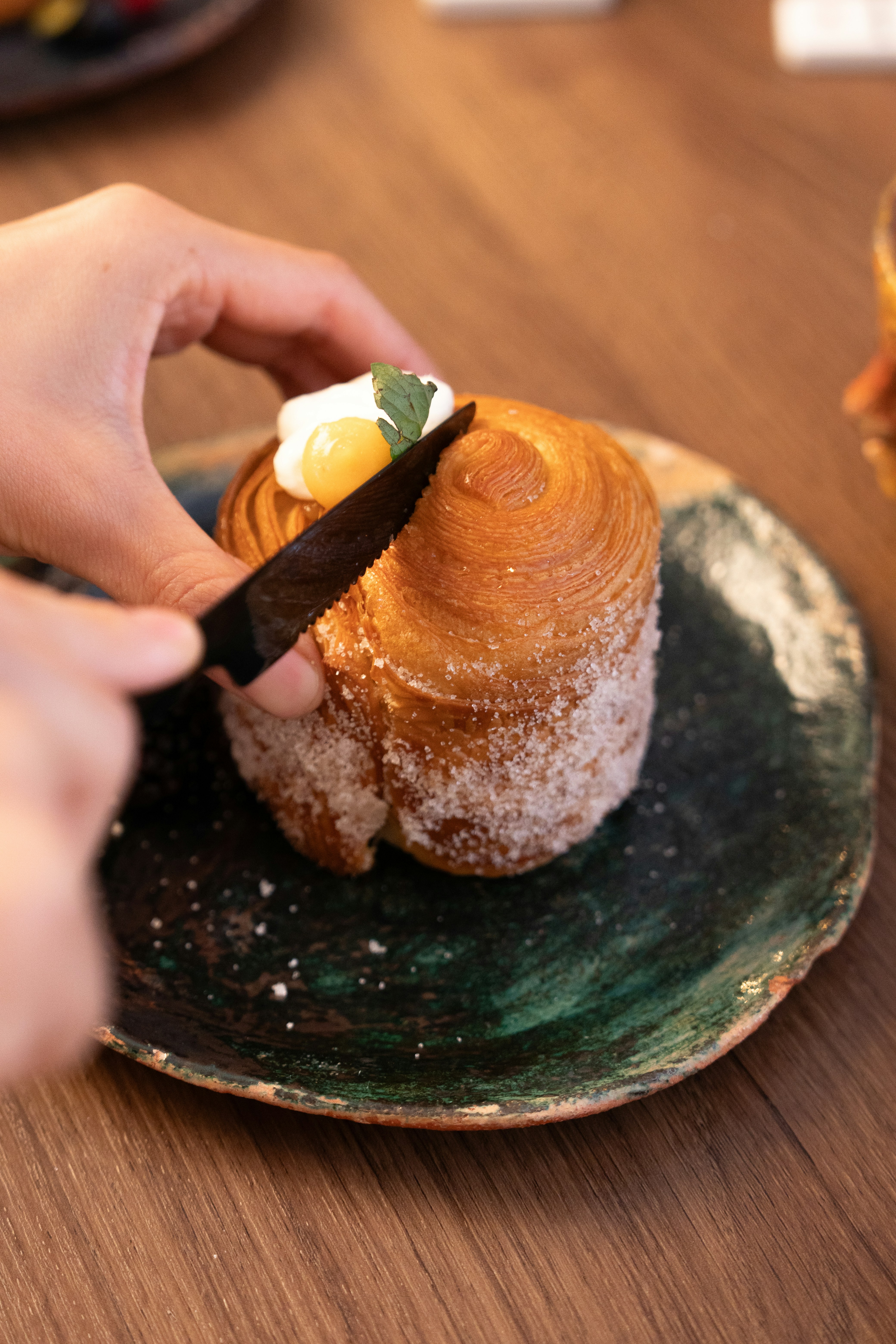 Hand cutting a croissant with cream and fruit topping.