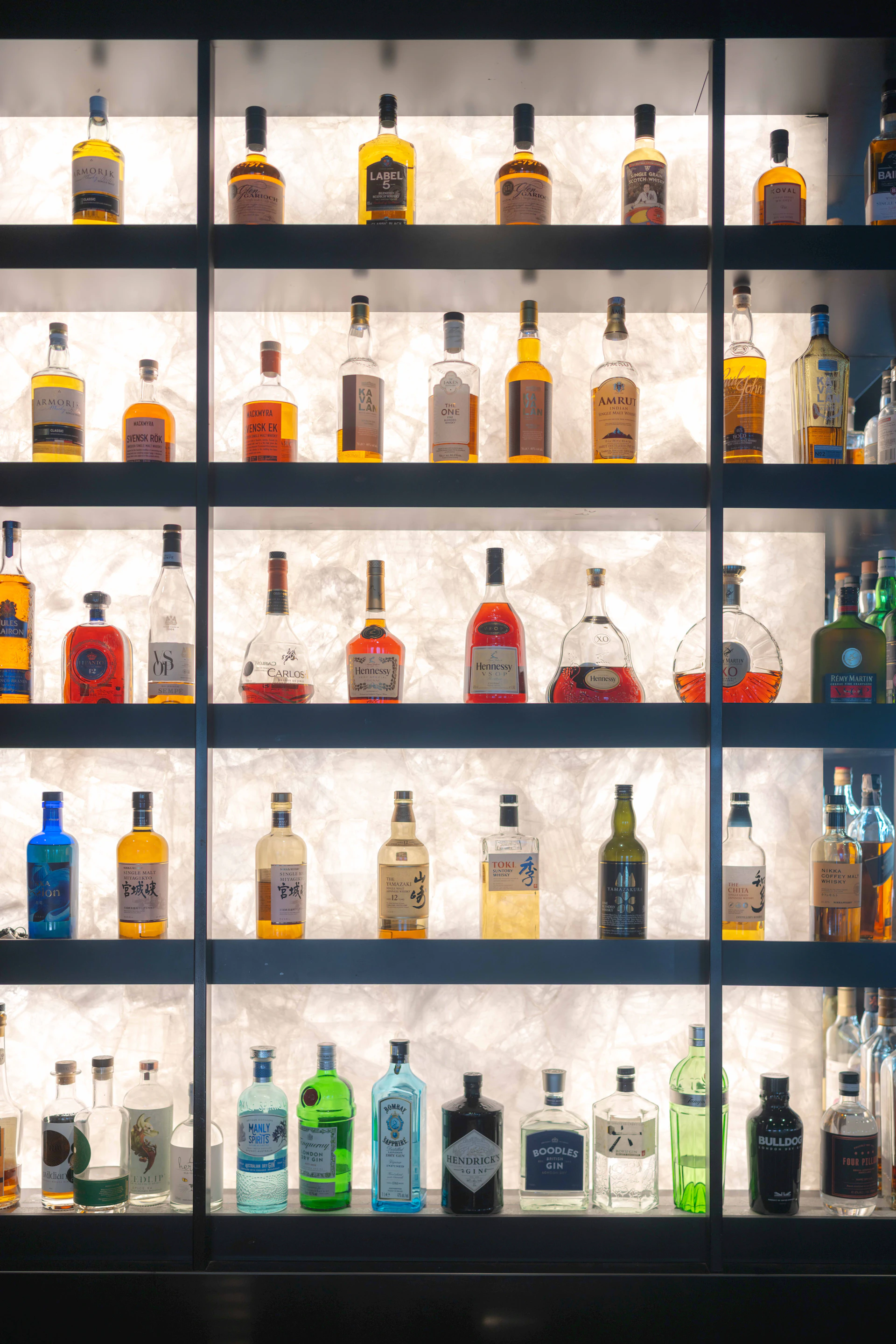 Illuminated shelves displaying rows of whisky bottles in a dark bar setting