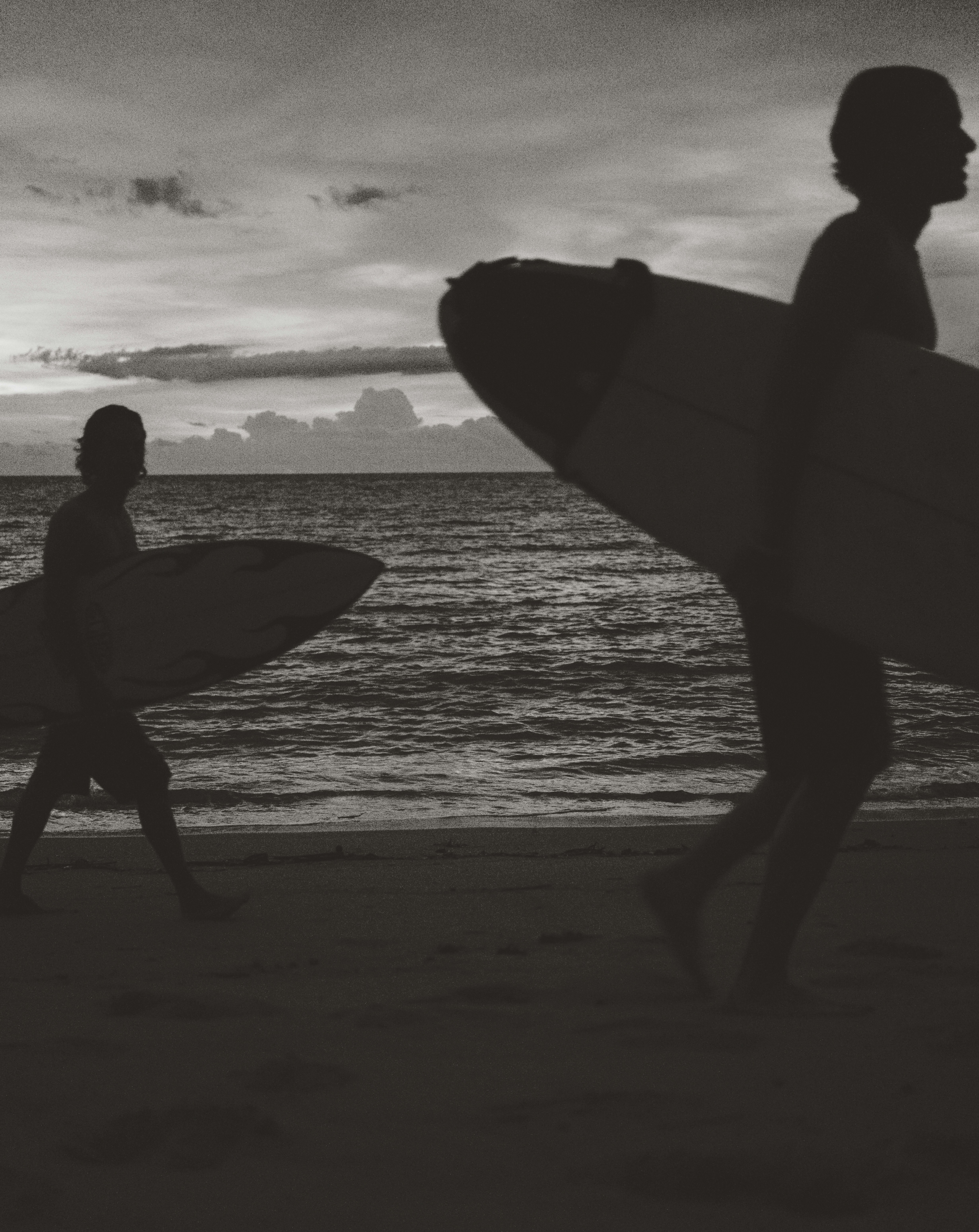 Two surfers walking on the beach at sunset
