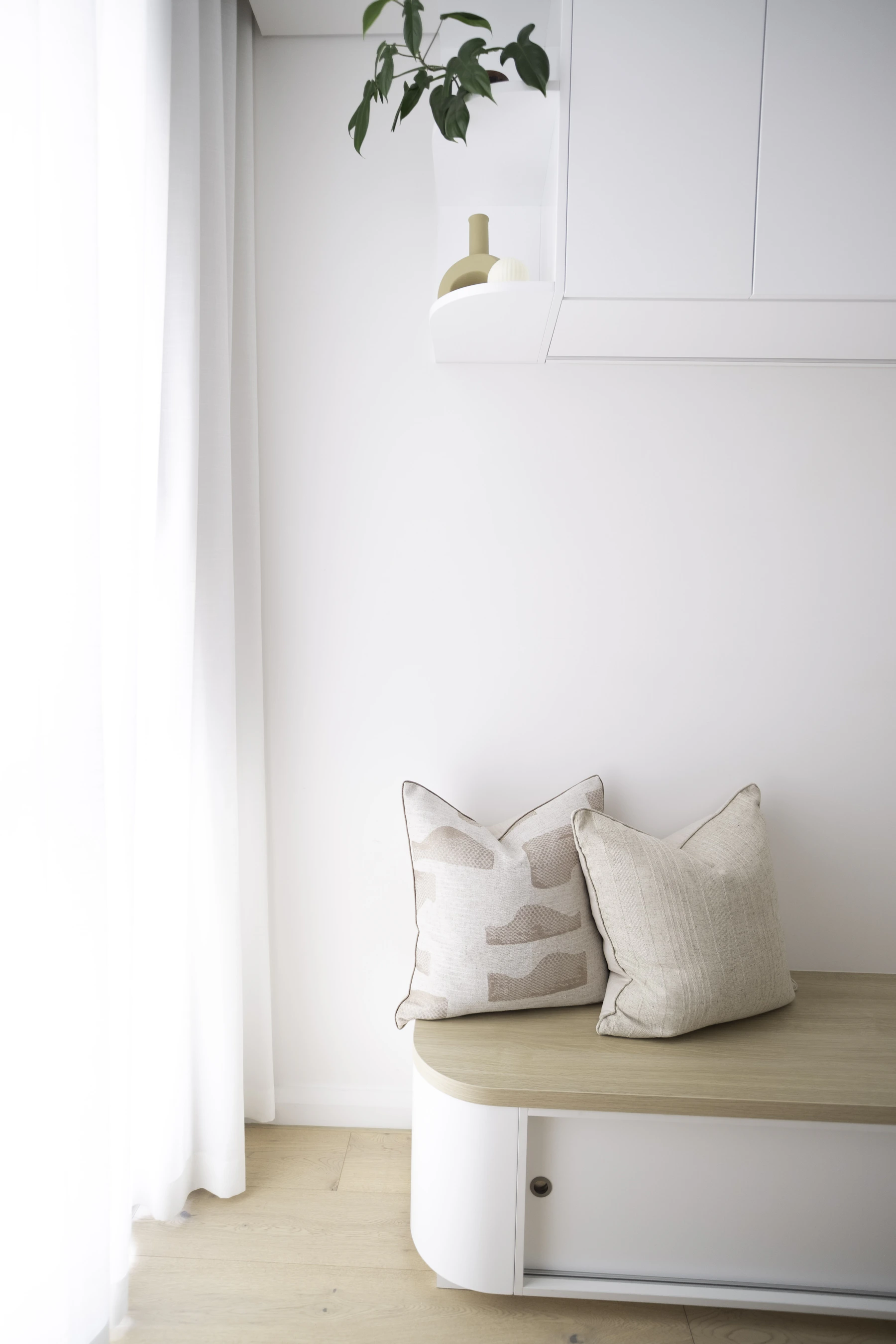Bright minimalist interior with natural timber bench, textured cushions and restrained decorative objects