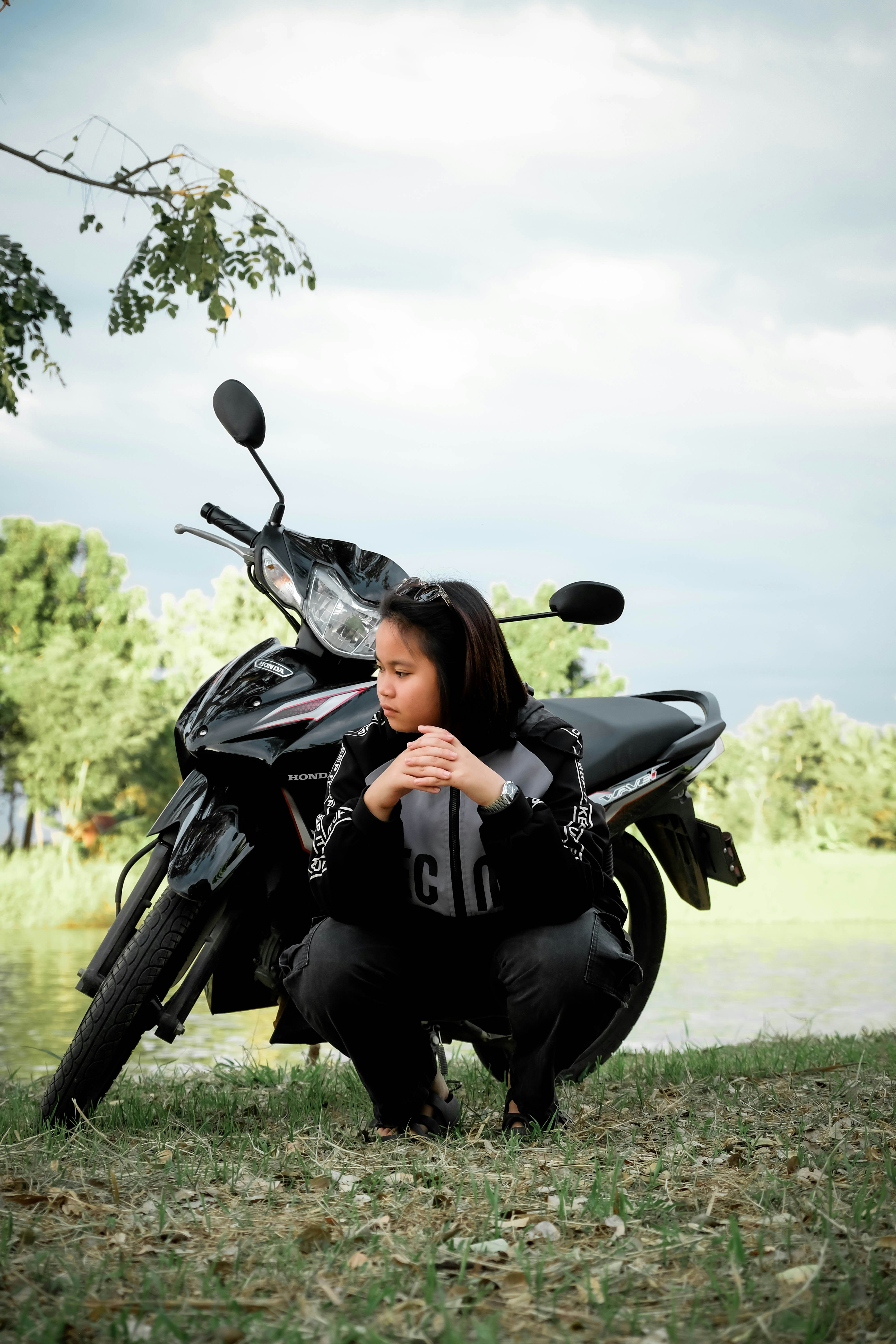 Un joven se agacha junto a una moto al aire libre.